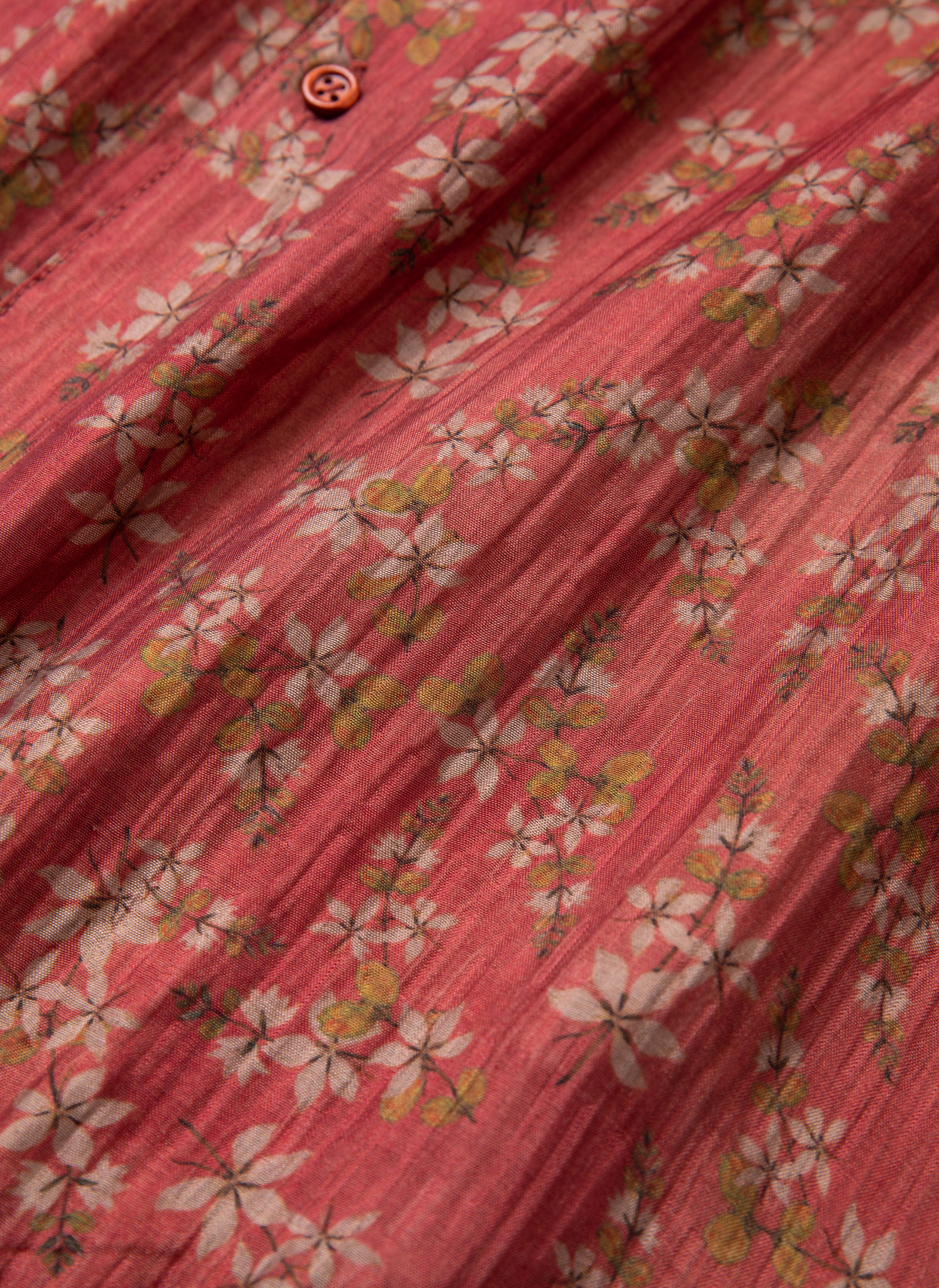 Close-up of the FOUND Charlot LS Camp Shirt, highlighting its red fabric adorned with a subtle white and green floral pattern, featuring dual chest pockets and a single red button near the top.