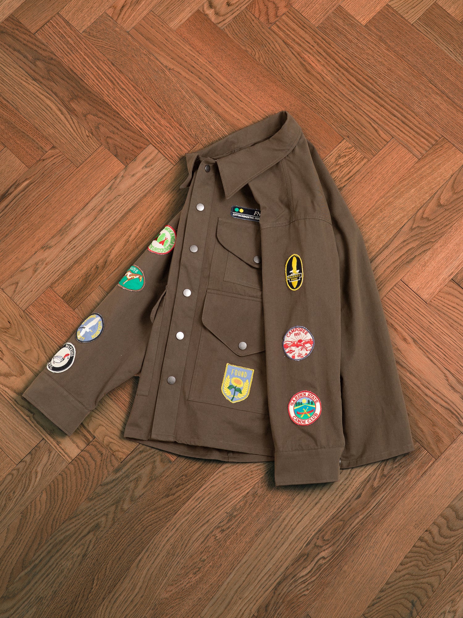 A brown vintage-inspired Found Ports Park Multi Patch Work Jacket with embroidered patches on the floor.