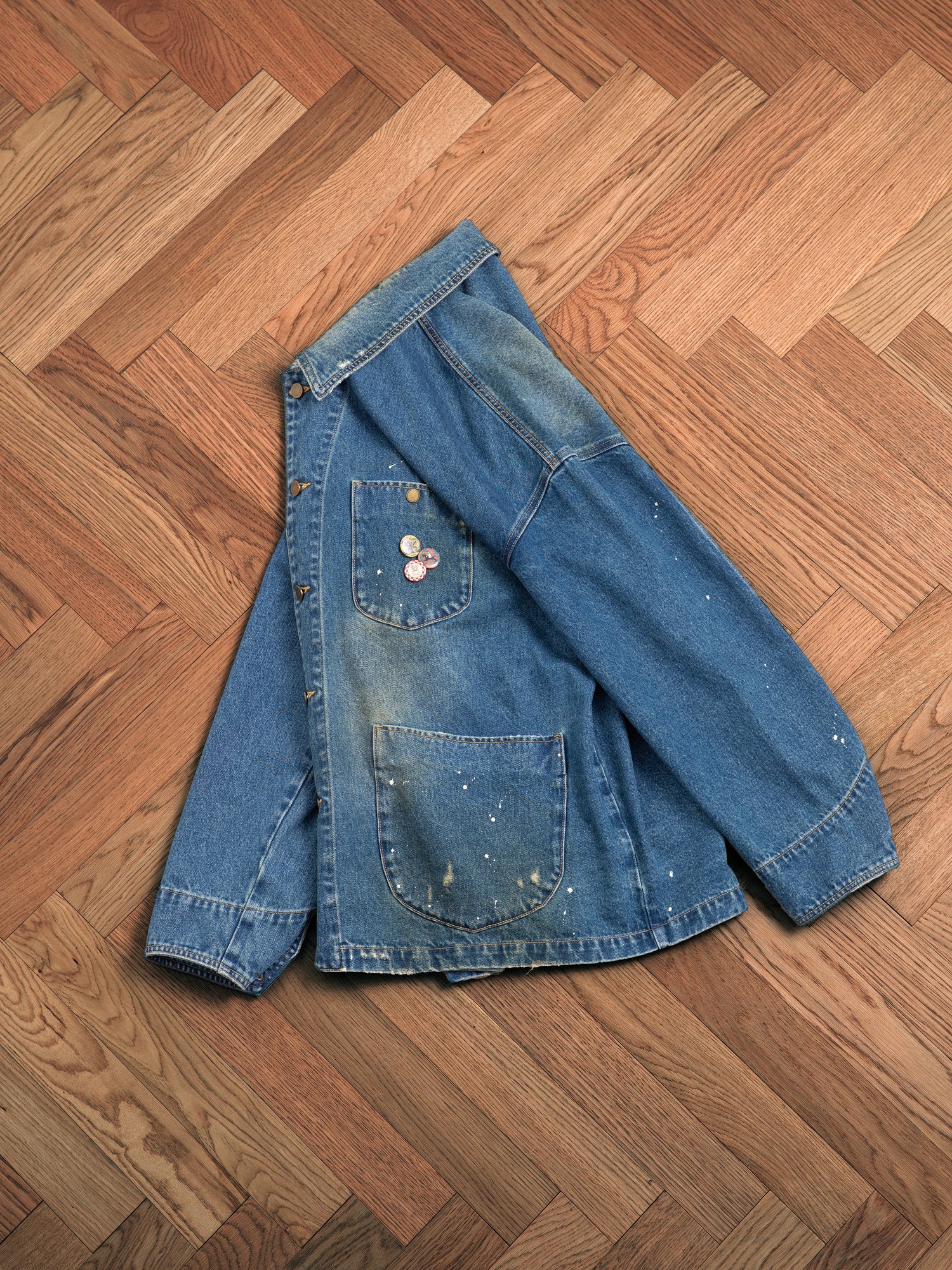 An artist's Kavir Denim Painter Jacket by Found laying on a wooden floor.