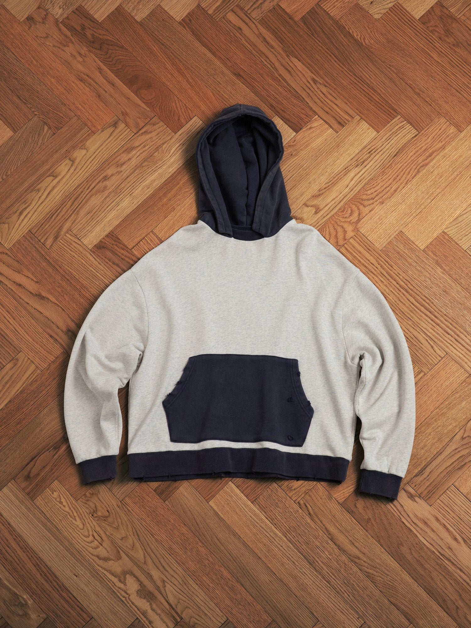 A **Found** two-tone hoodie with a pocket on a wooden floor.