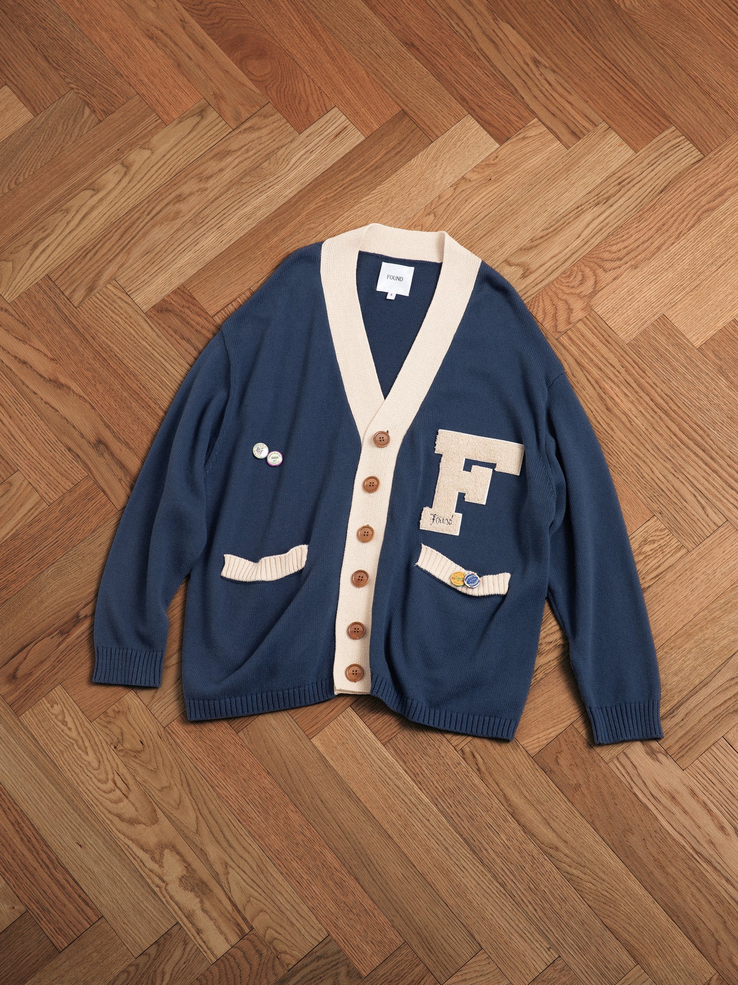 A blue and white Found Varsity Contrast Cardigan sitting on a wooden floor.