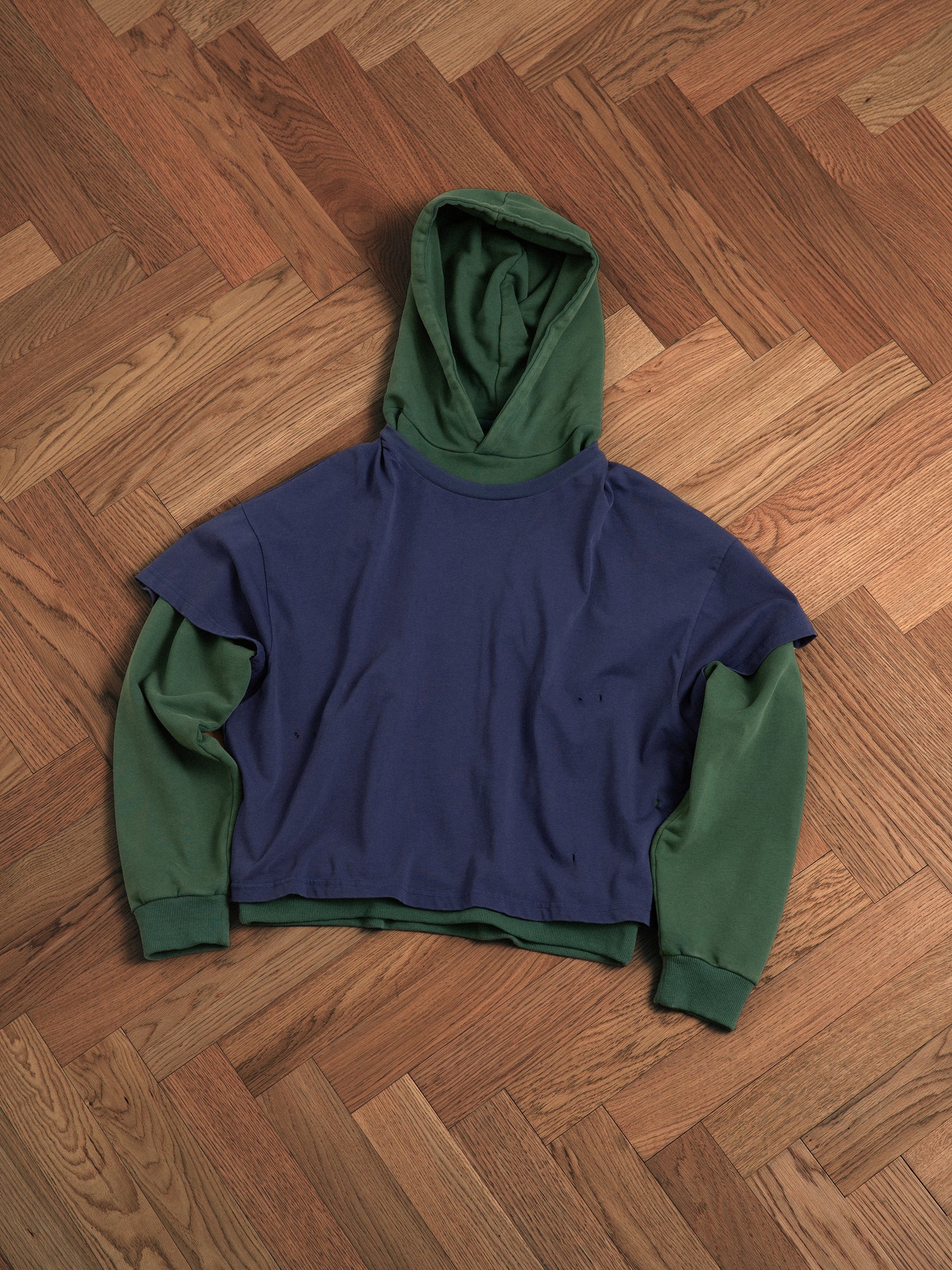 A blue and green Found double layer hoodie on a hardwood floor.