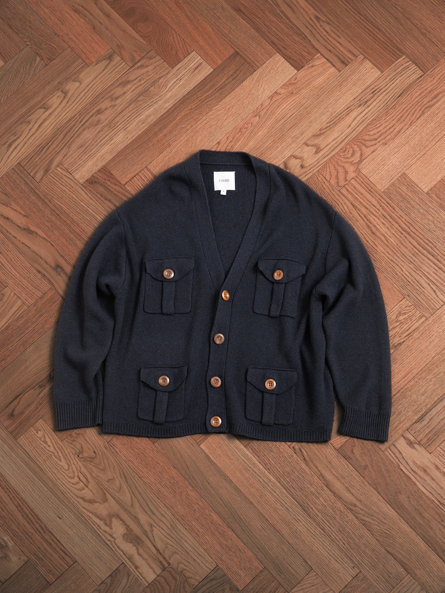 A navy knit fabric Found Lighthouse Multi Pocket Cardigan sitting on a wooden floor.