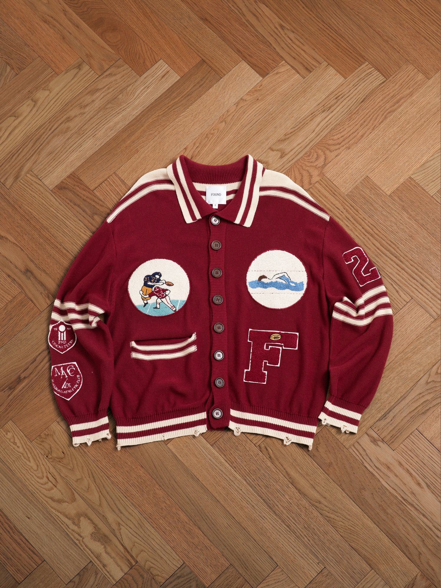 A maroon sweater with embroidered chenille patches on it, embracing the vintage Ivy League fashion, from Found featuring the Fin Varsity Patch Collared Cardigan.