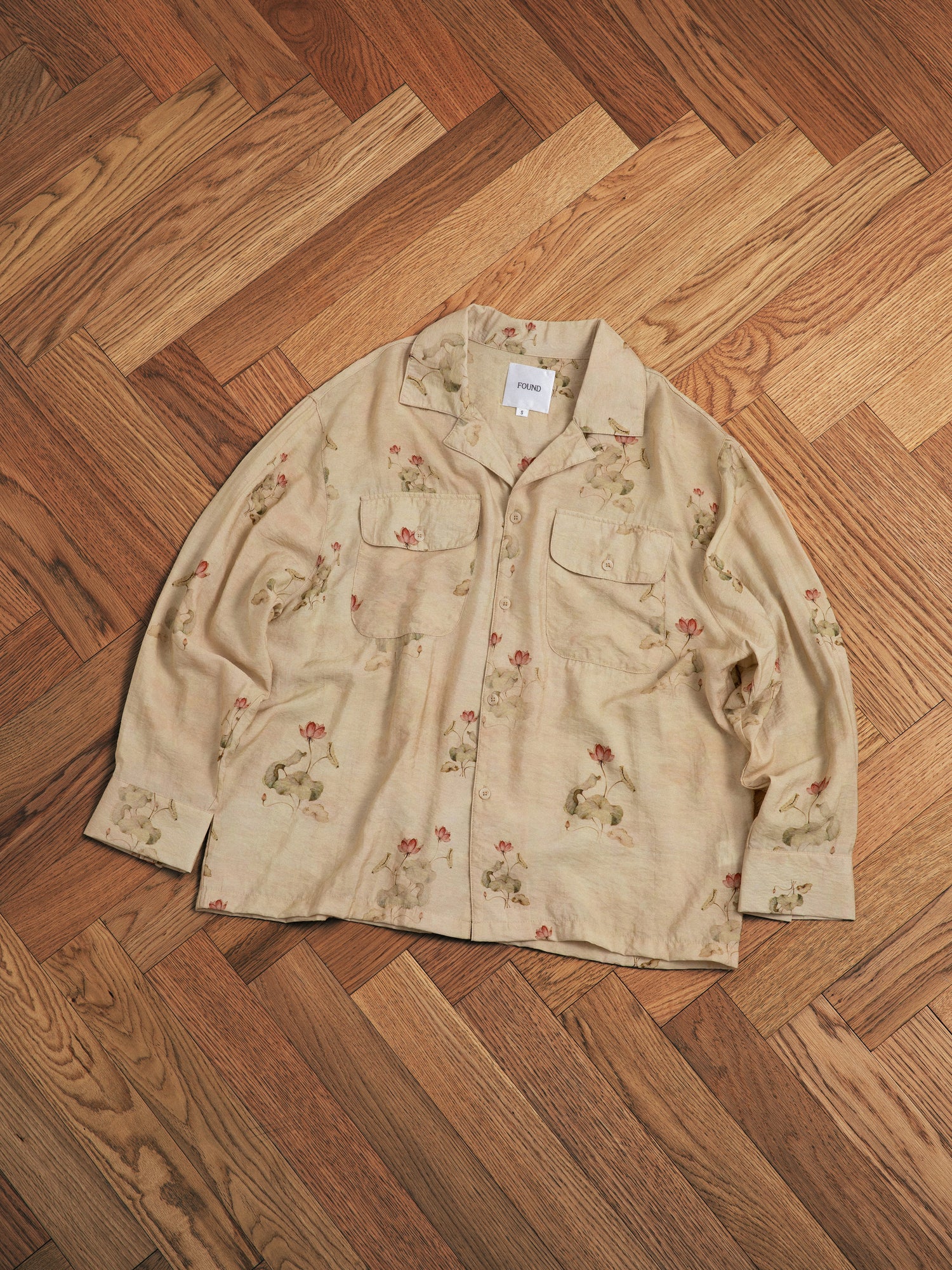A Found Lotus LS Camp Shirt with flowers on it is sitting on a hardwood floor.
