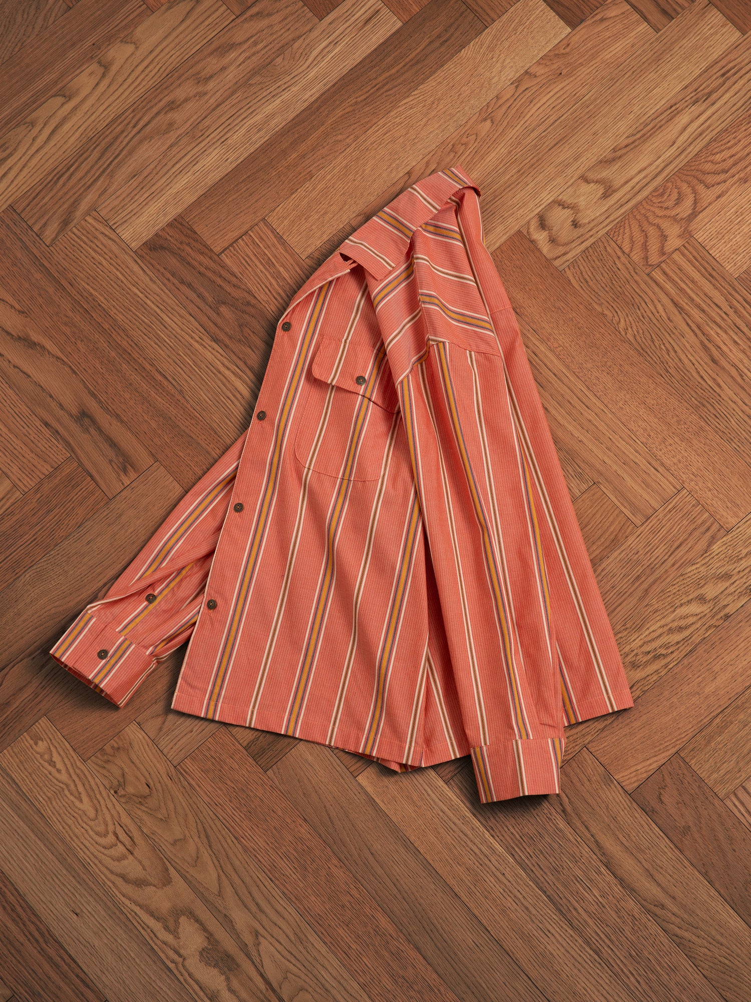 A classic appeal Found Orange Stripe Citrus LS Camp Shirt laying on a wooden floor, creating a timeless silhouette.