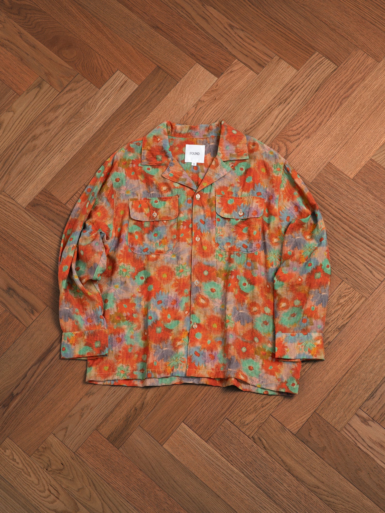A Found Waterblend LS Camp Shirt with orange floral patterns adds classic appeal, resting on a hardwood floor.