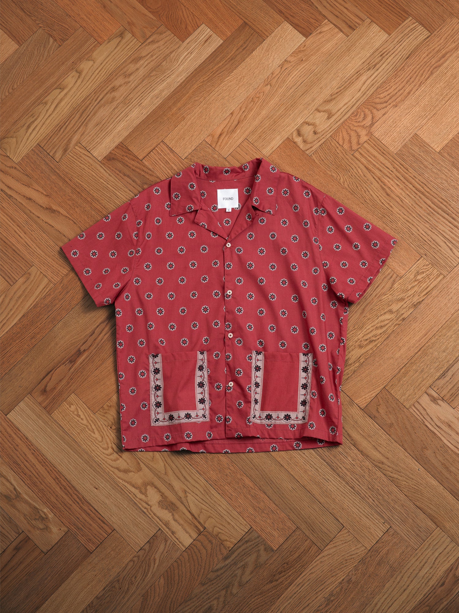 A Found Red Motif SS Camp Shirt on a wooden floor.