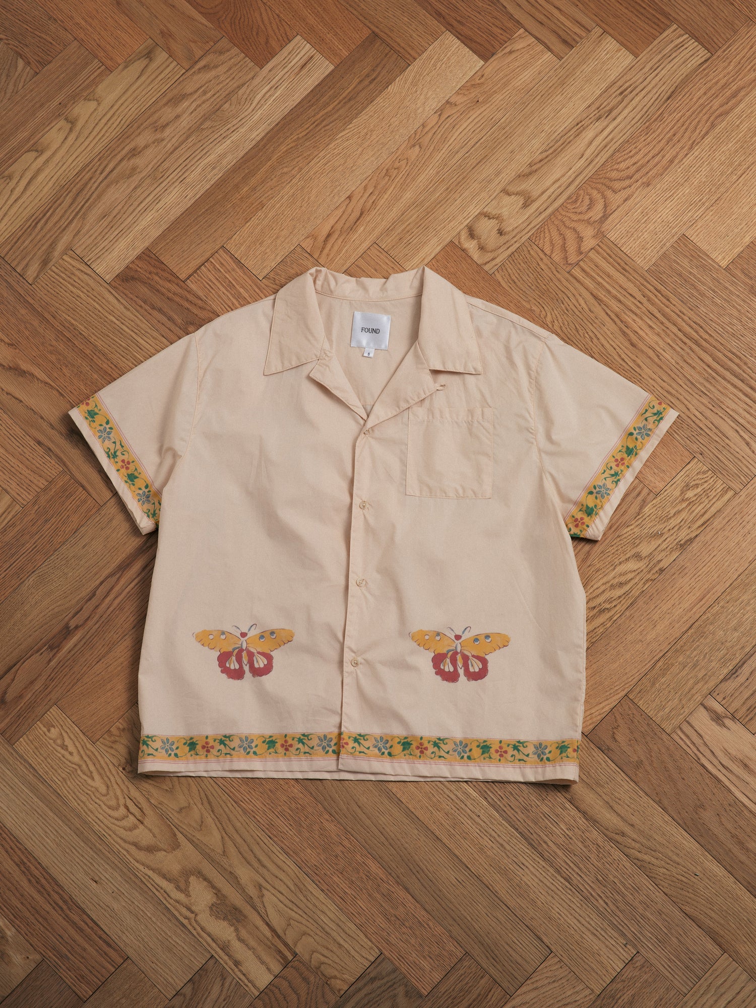 A beige shirt with embroidered butterflies and Phulkari motifs on it.