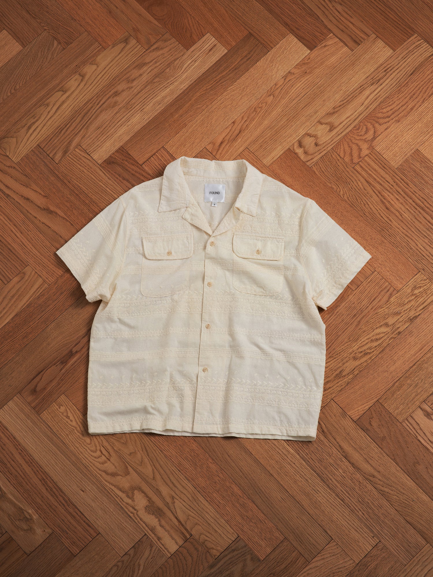A Found Lace SS Camp Shirt with delicate lace detailing on a wooden floor.