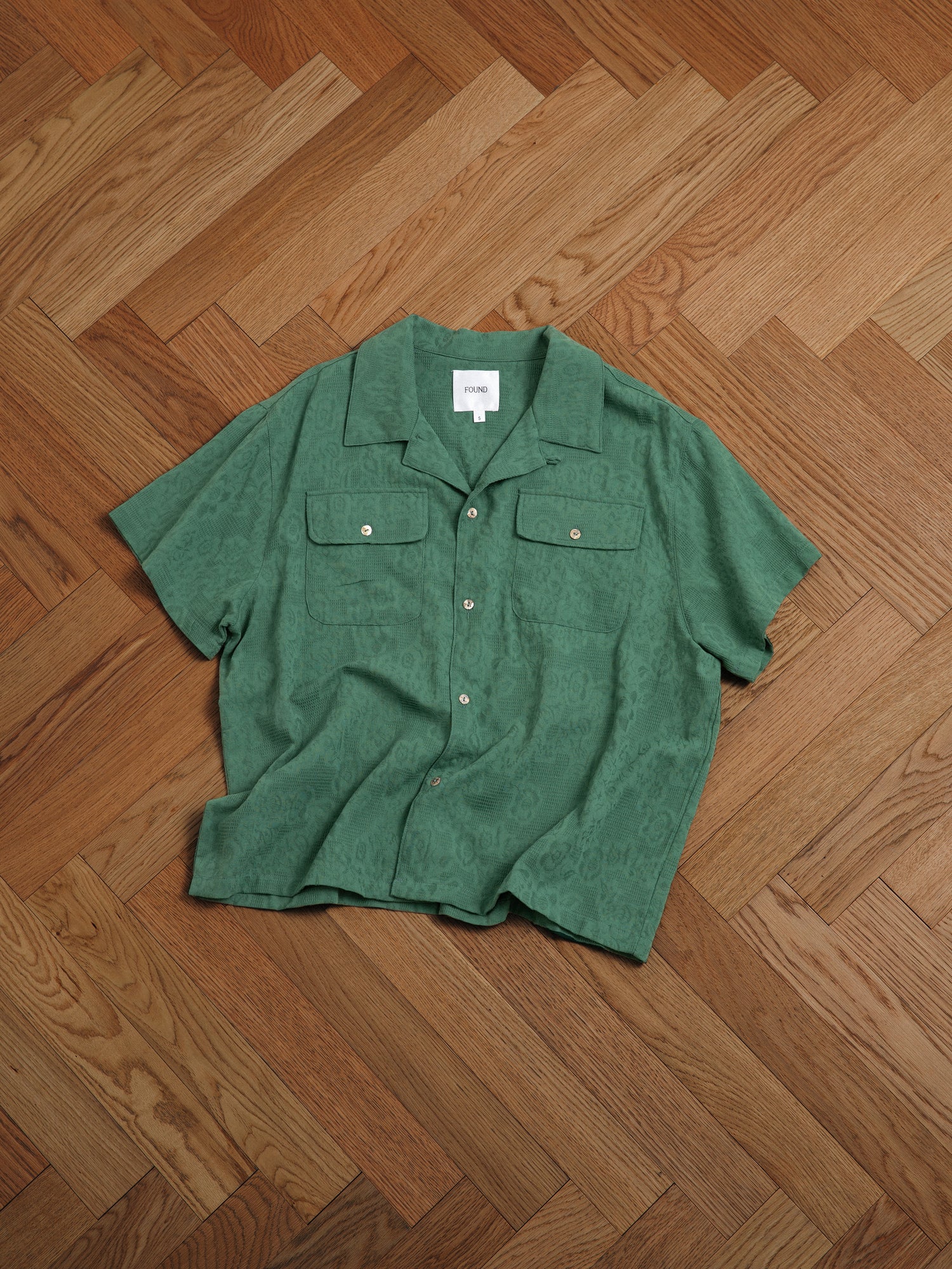 A premium cotton Mount Camp Shirt by Found with lace detailing laying on a wooden floor.