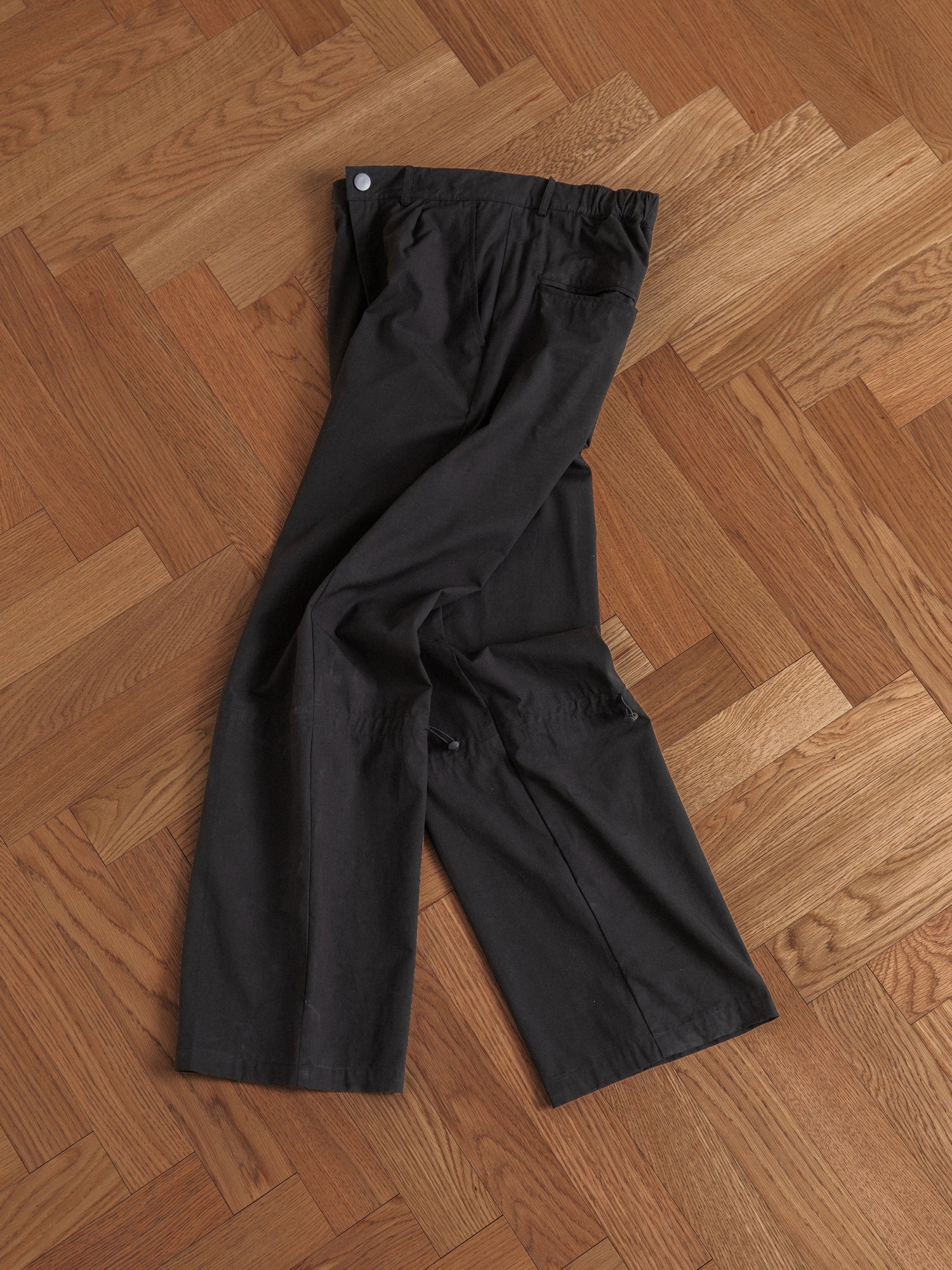 Black Tencel pleated pants from Found laid flat on a herringbone wooden floor.