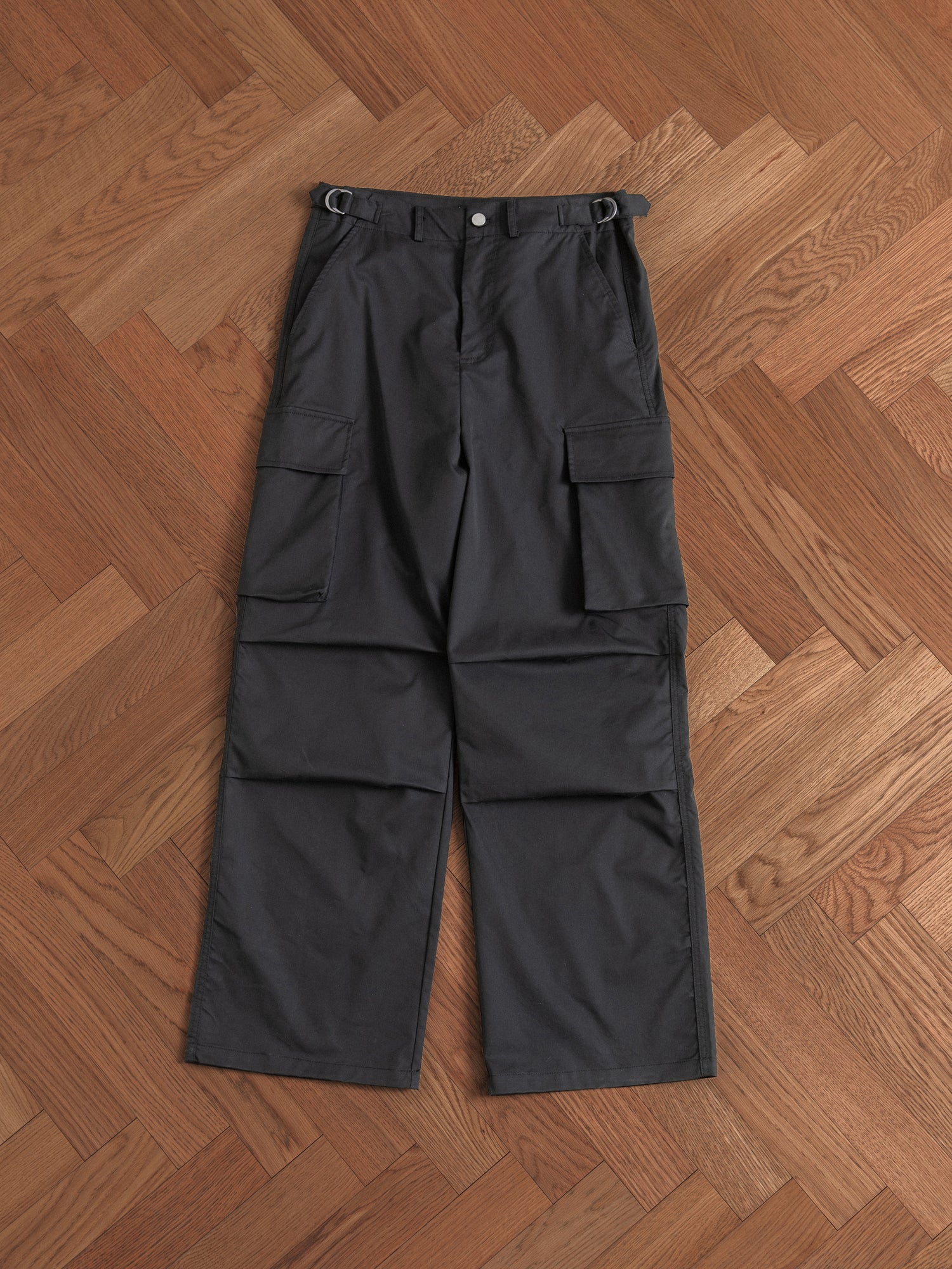 A pair of Found Elbas Cargo Pants with adjustable waist tabs on a hardwood floor.