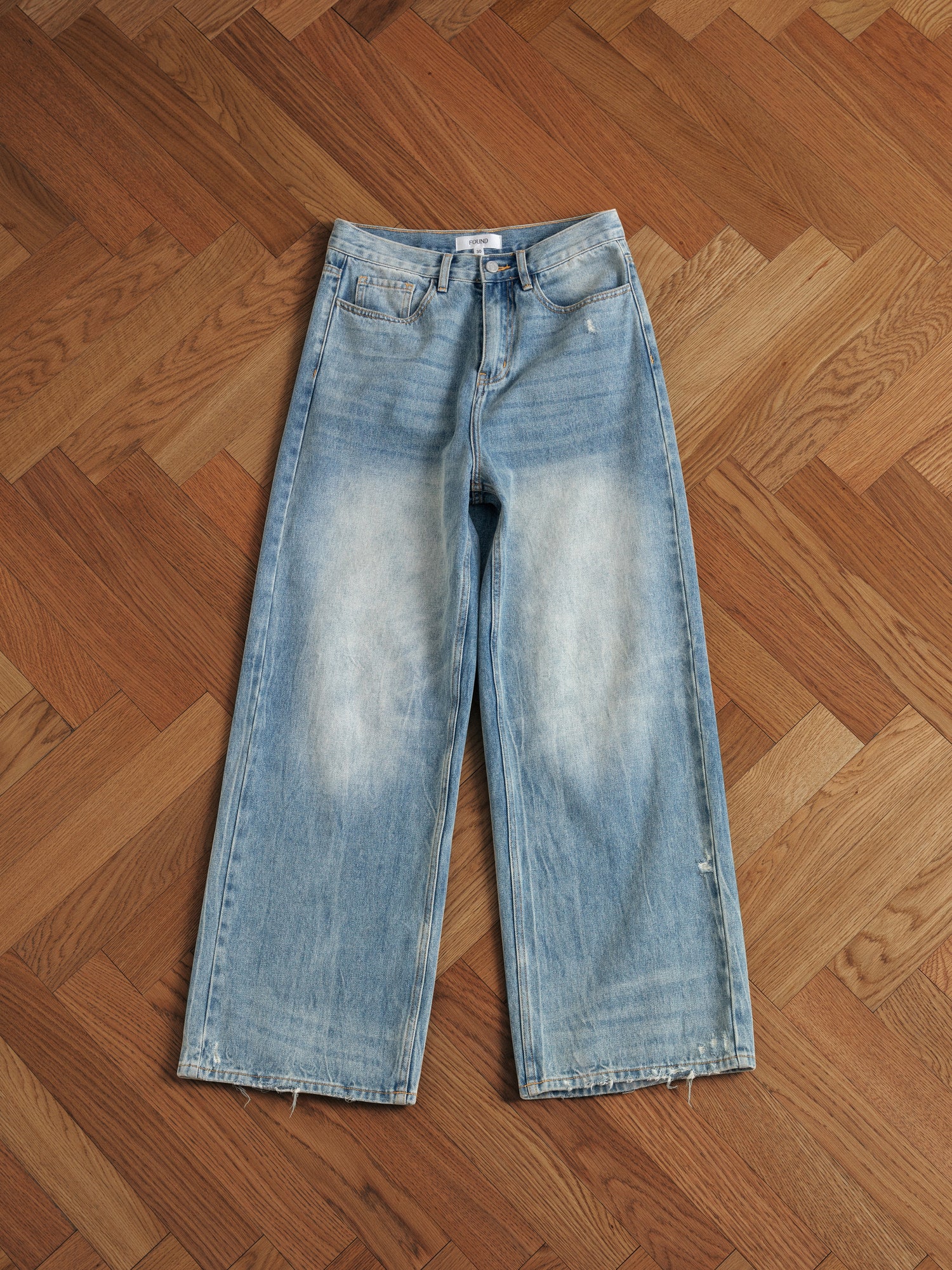 A pair of Found Lacy Baggy Jeans sitting on a wooden floor.