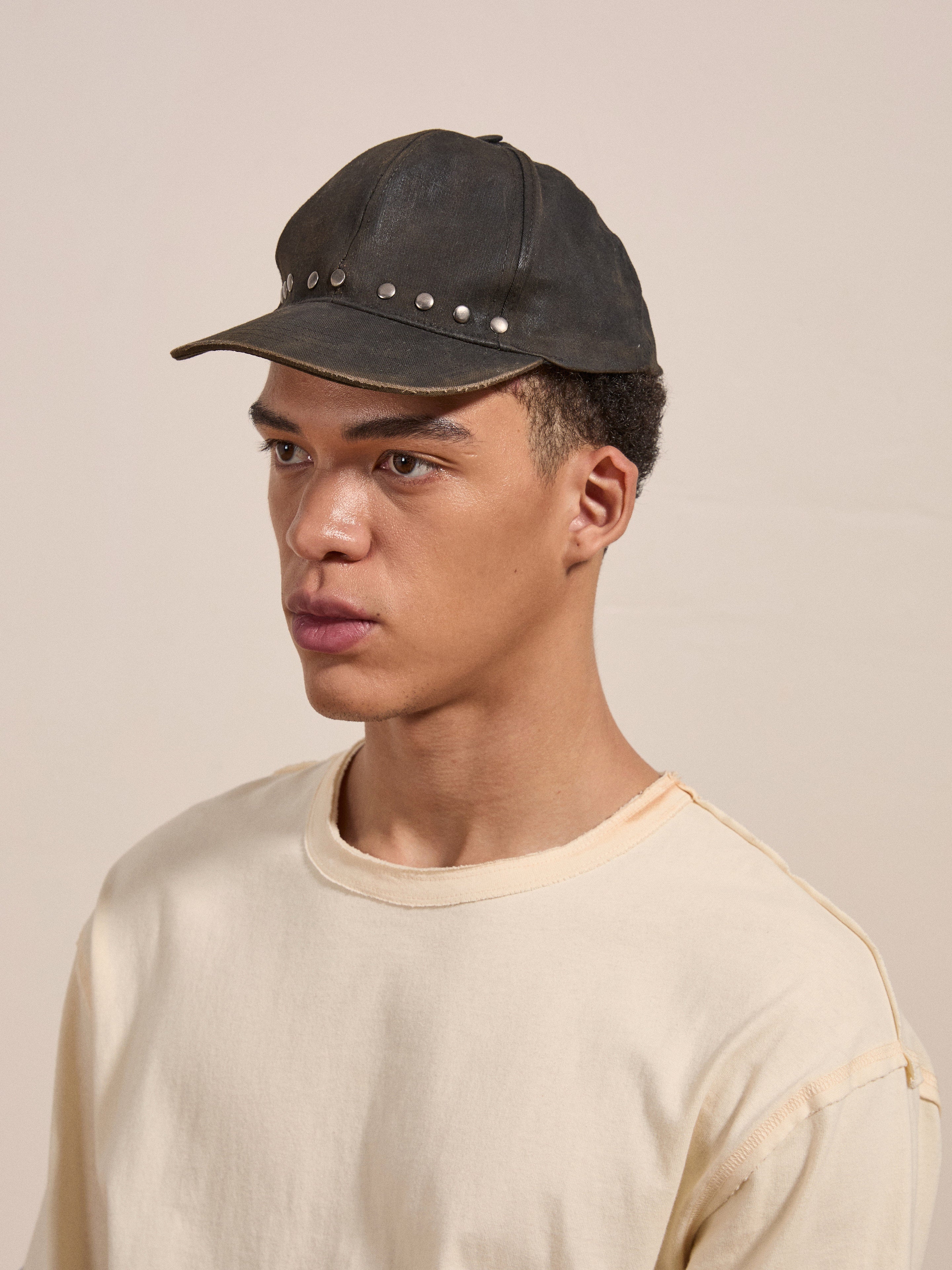 A person wearing a white t-shirt and a FOUND Waxed Charcoal Studded Cap is looking towards the left against a plain background.