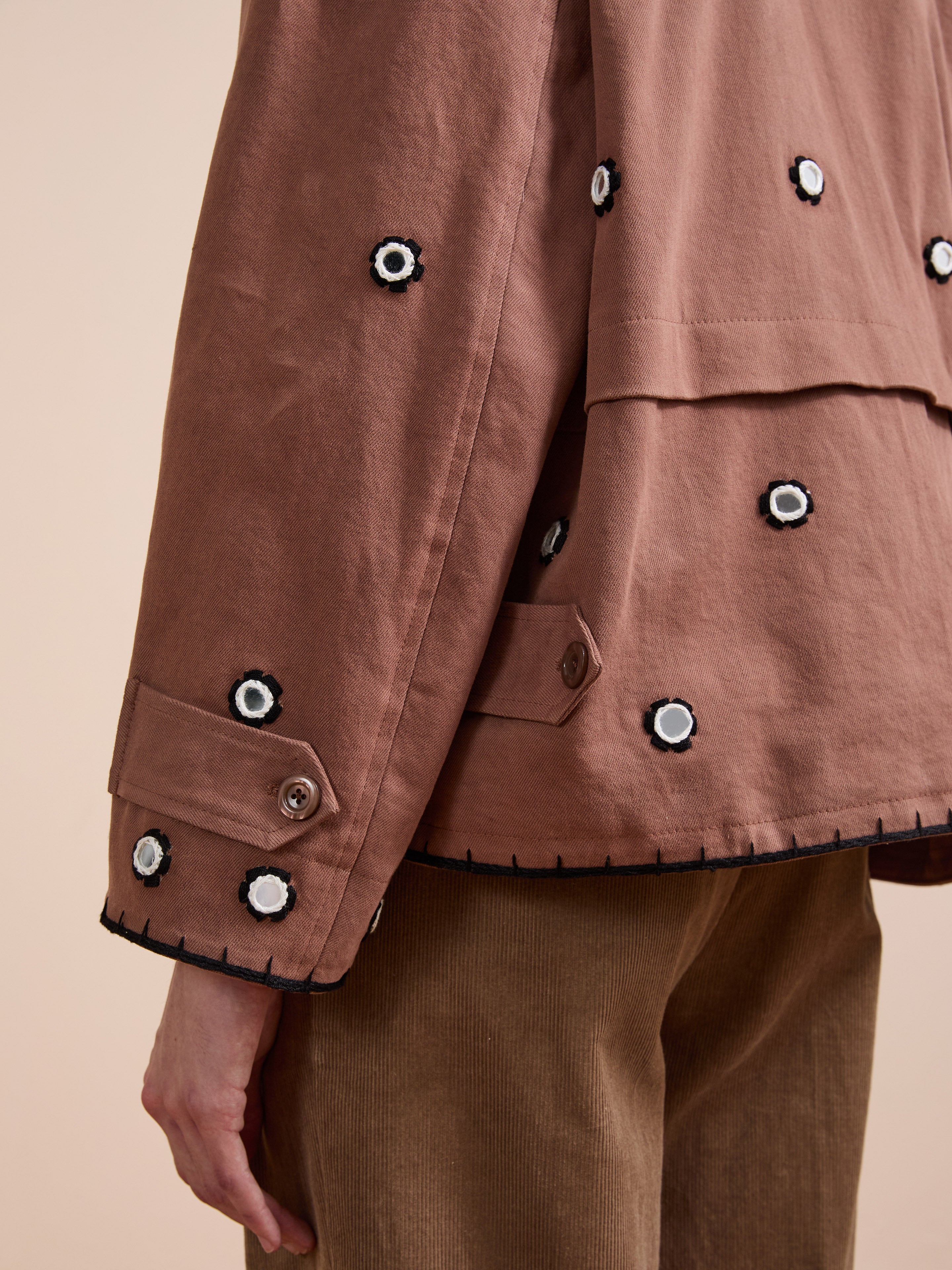 A close-up of a person wearing the FOUND Hand Embroidered Hooded Mirror Anorak, featuring small black and white floral appliqués, button details, and subtle mirror embroidery, paired with brown corduroy pants.