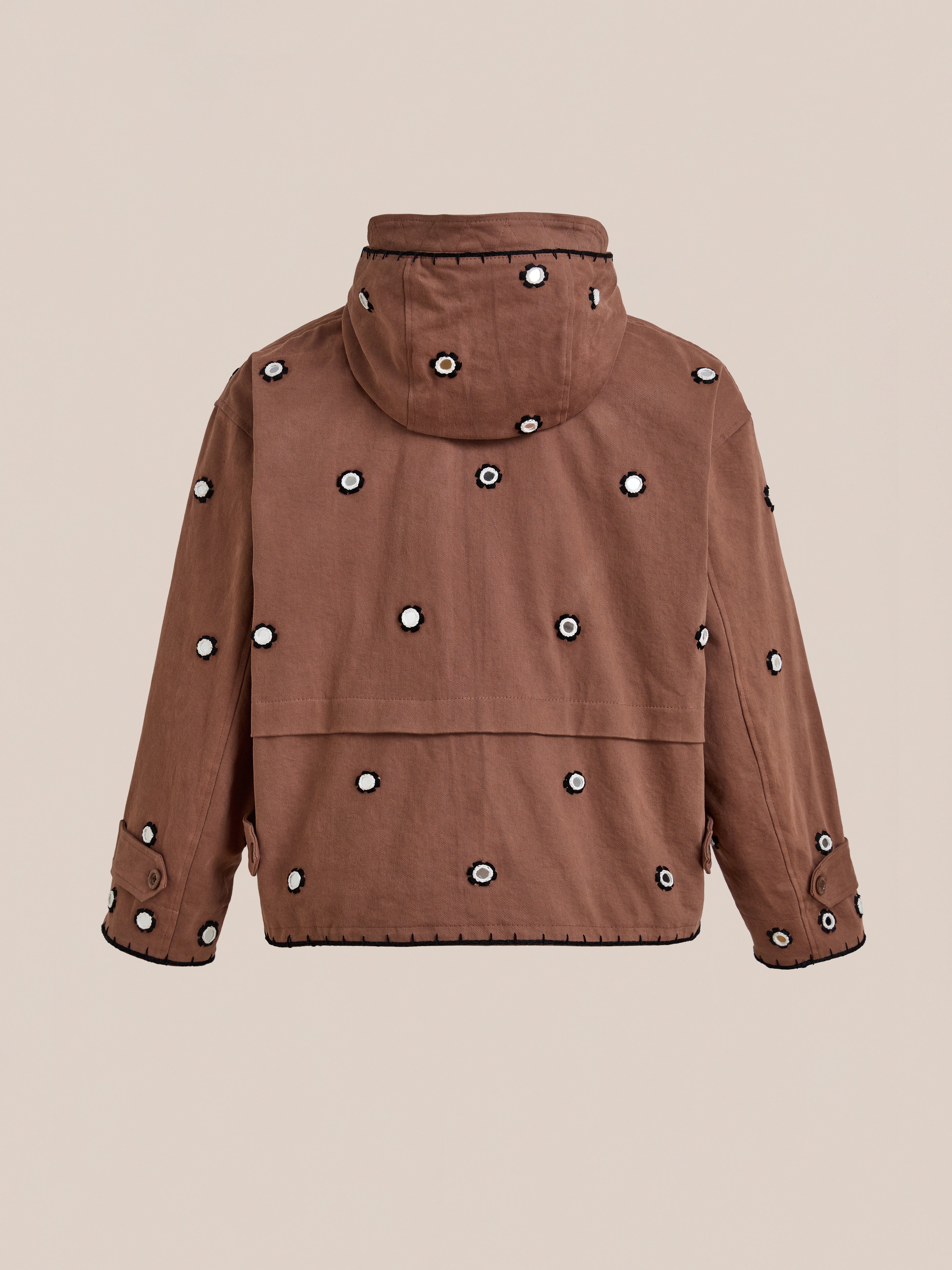 The FOUND Hand Embroidered Hooded Mirror Anorak features brown cotton twill with black and white circular mirror embroidery patches on the back, sleeves, and hood, shown against a plain beige background.