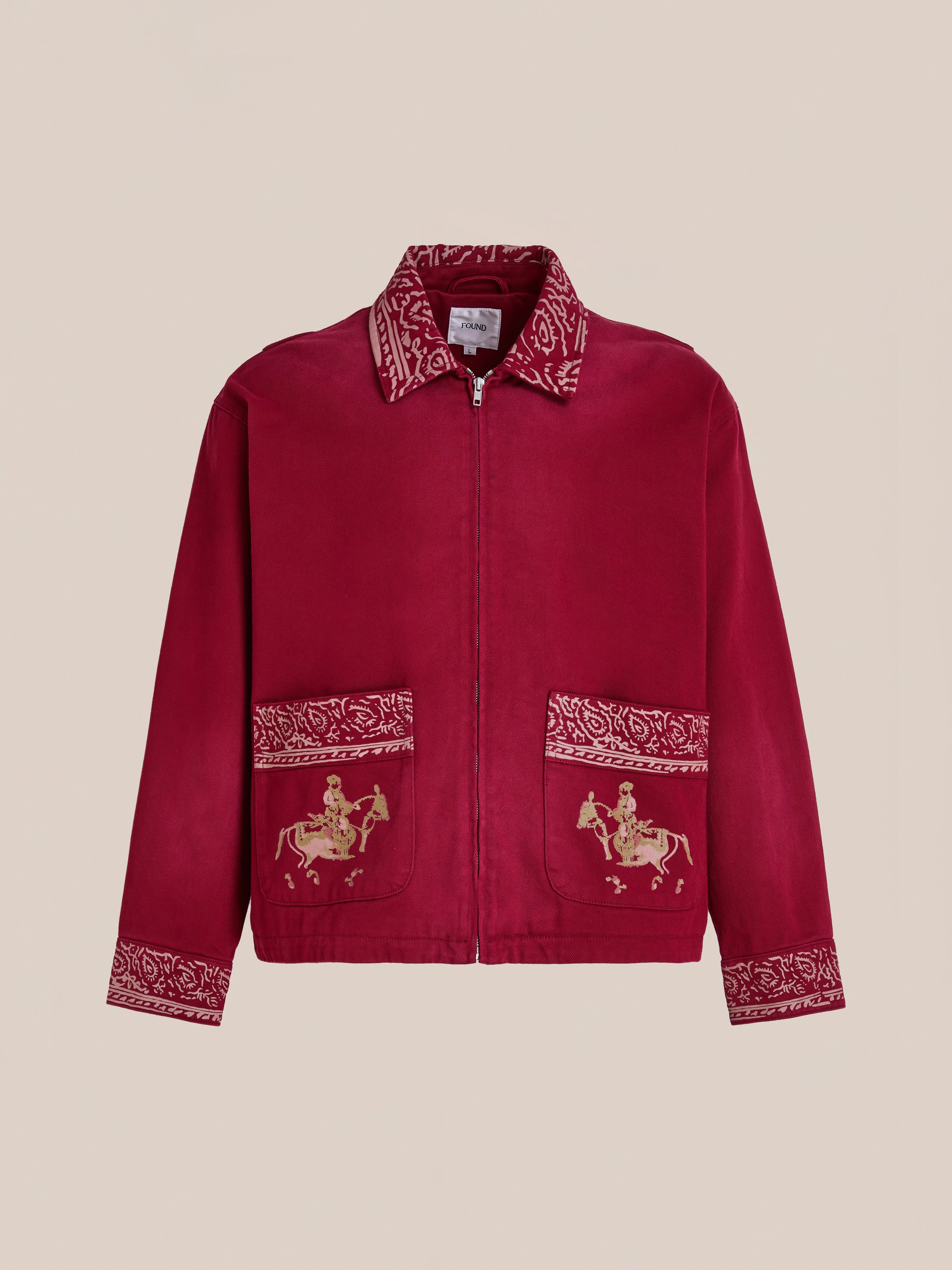 The Abhala Printed Work Jacket by Found is a bold unisex red jacket featuring a front zipper, patterned cuffs and collar, and two pockets with embroidered horse and rider equestrian motifs.