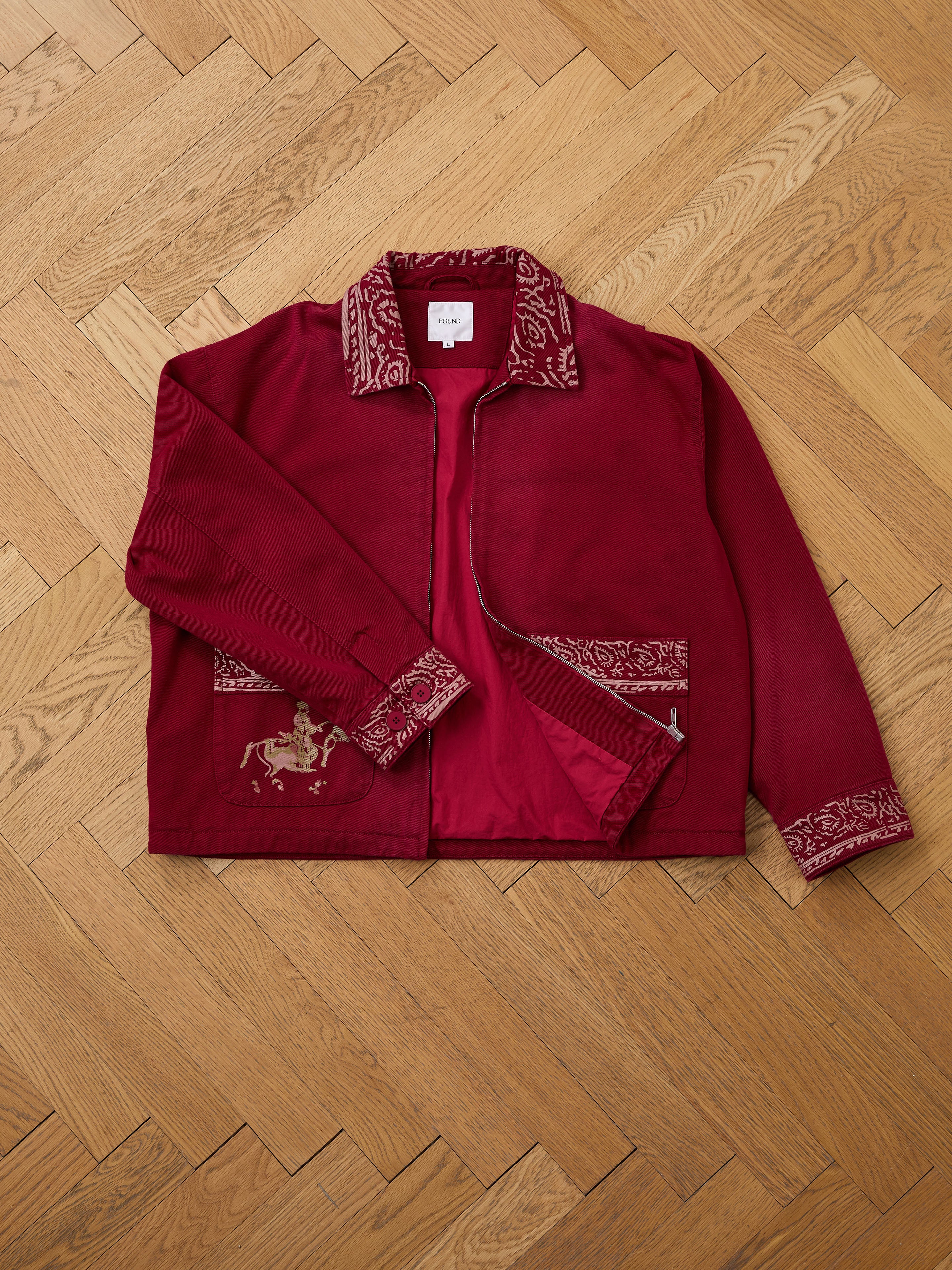 The Found Abhala Printed Work Jacket is a unisex red jacket with decorative embroidery and equestrian horse and rider motifs on the collar, cuffs, and pockets.