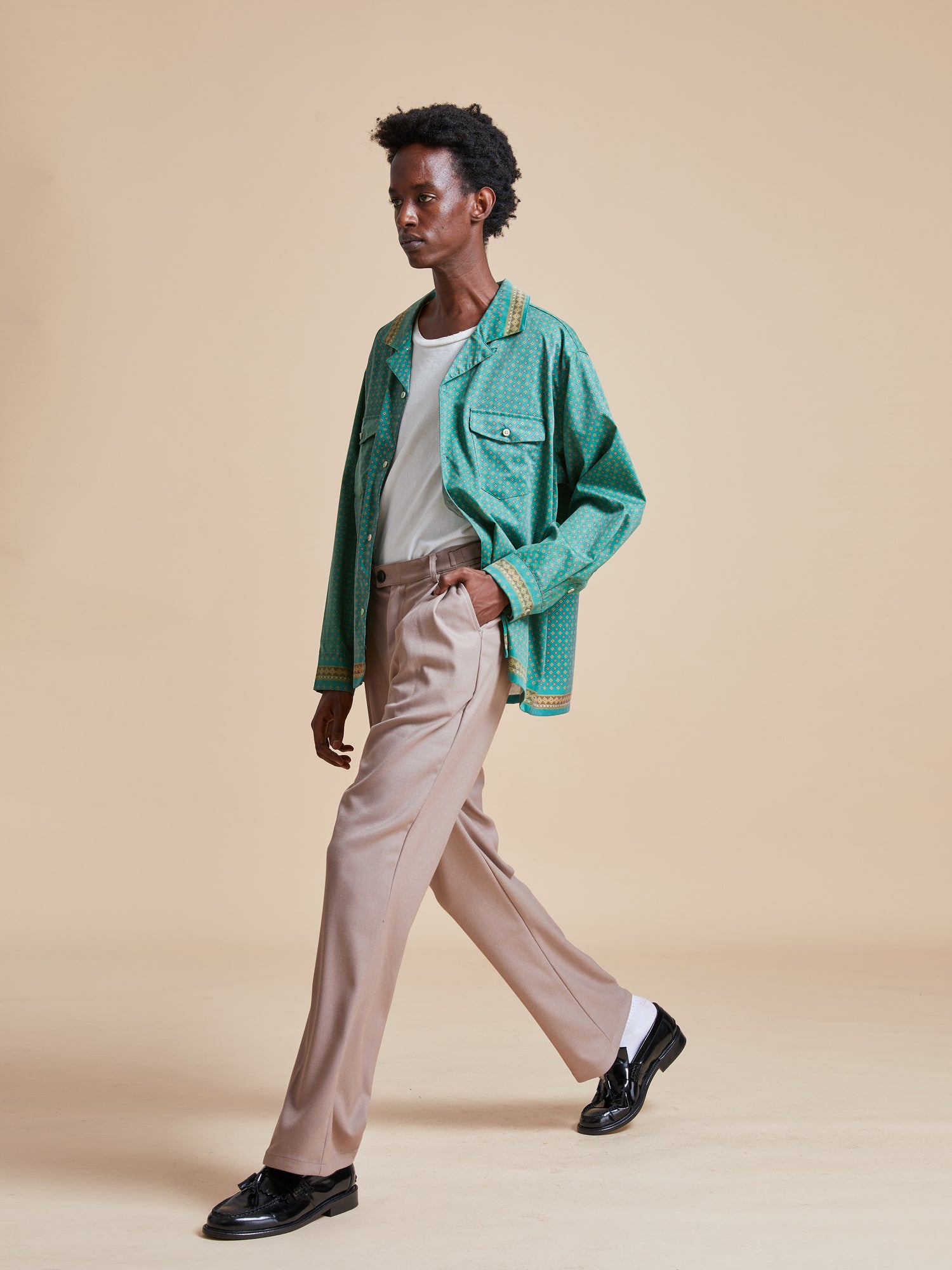 A woman in a green jacket walking on a beige background, showcasing the Found Arbor Long Sleeve Camp Shirt.