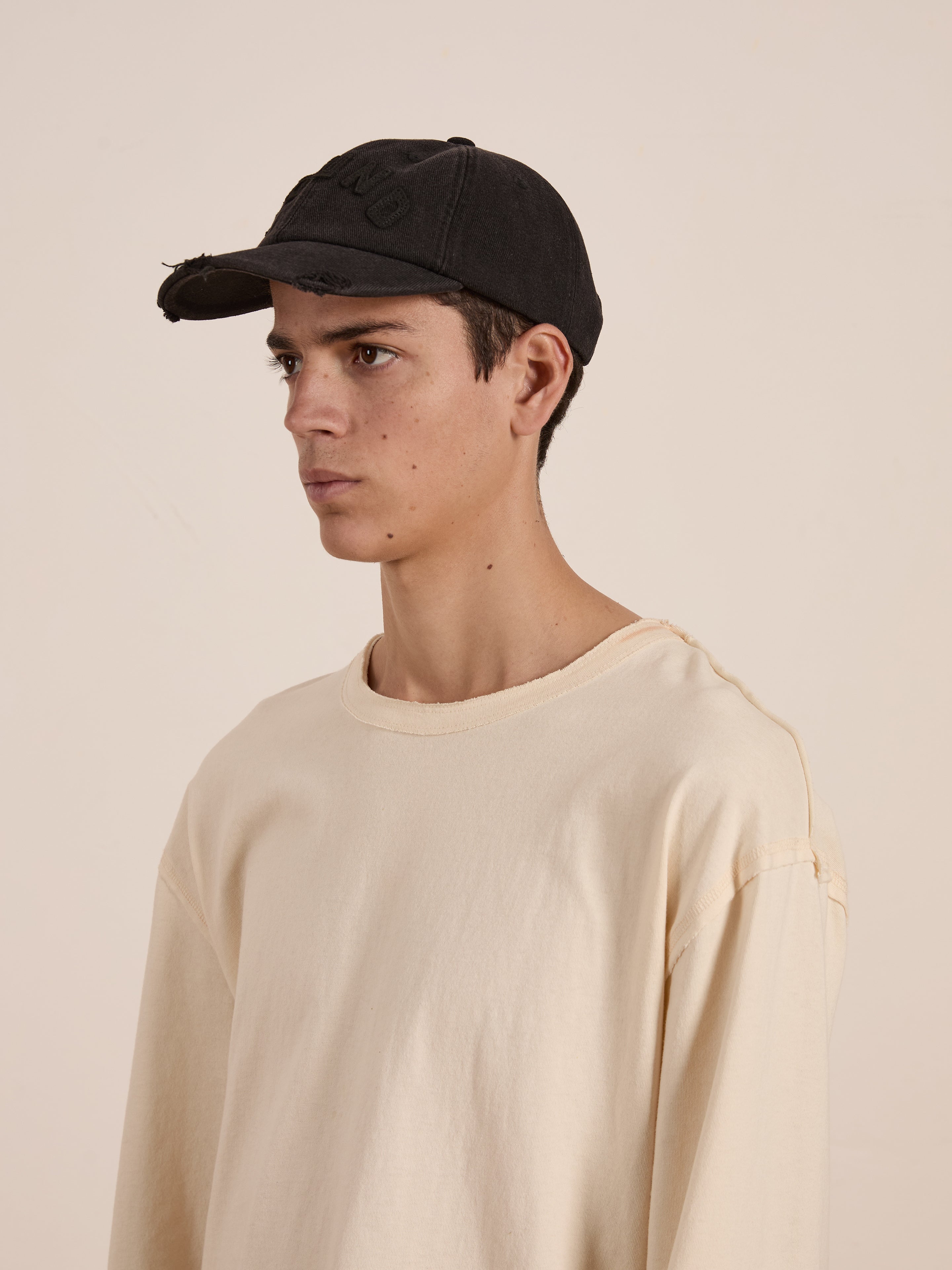 A person in a FOUND Black Felt Patch Cap, featuring a vintage washed black style with a hand-distressed brim, wears a beige long-sleeve shirt and looks to the side against a plain backdrop.