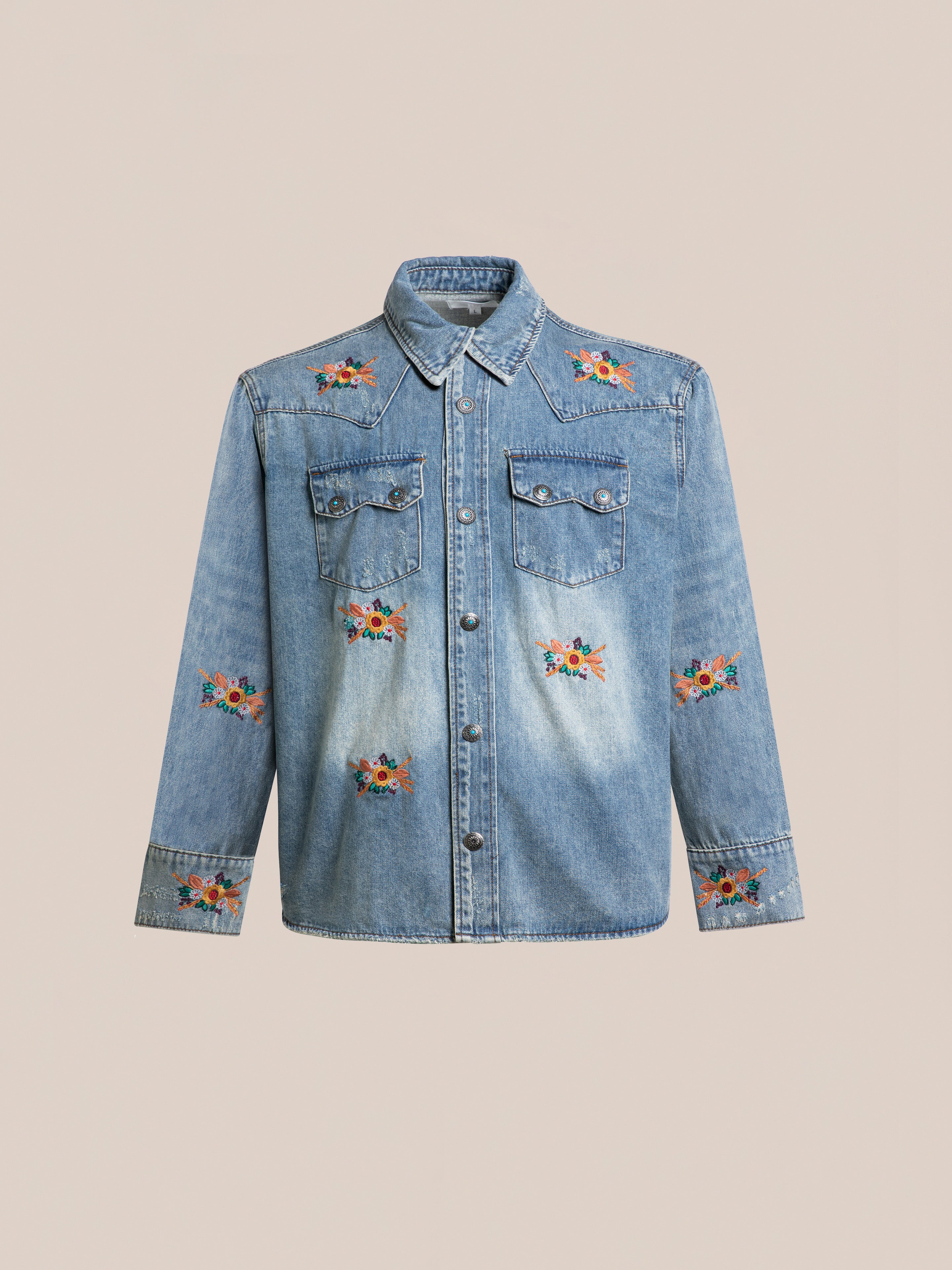 The FOUND Bouquet Floral Embroidered Western Denim Shirt features light blue denim, a relaxed fit, front buttons, chest pockets, and vibrant floral embroidery on the shoulders, pockets, front, and sleeves against a plain background.