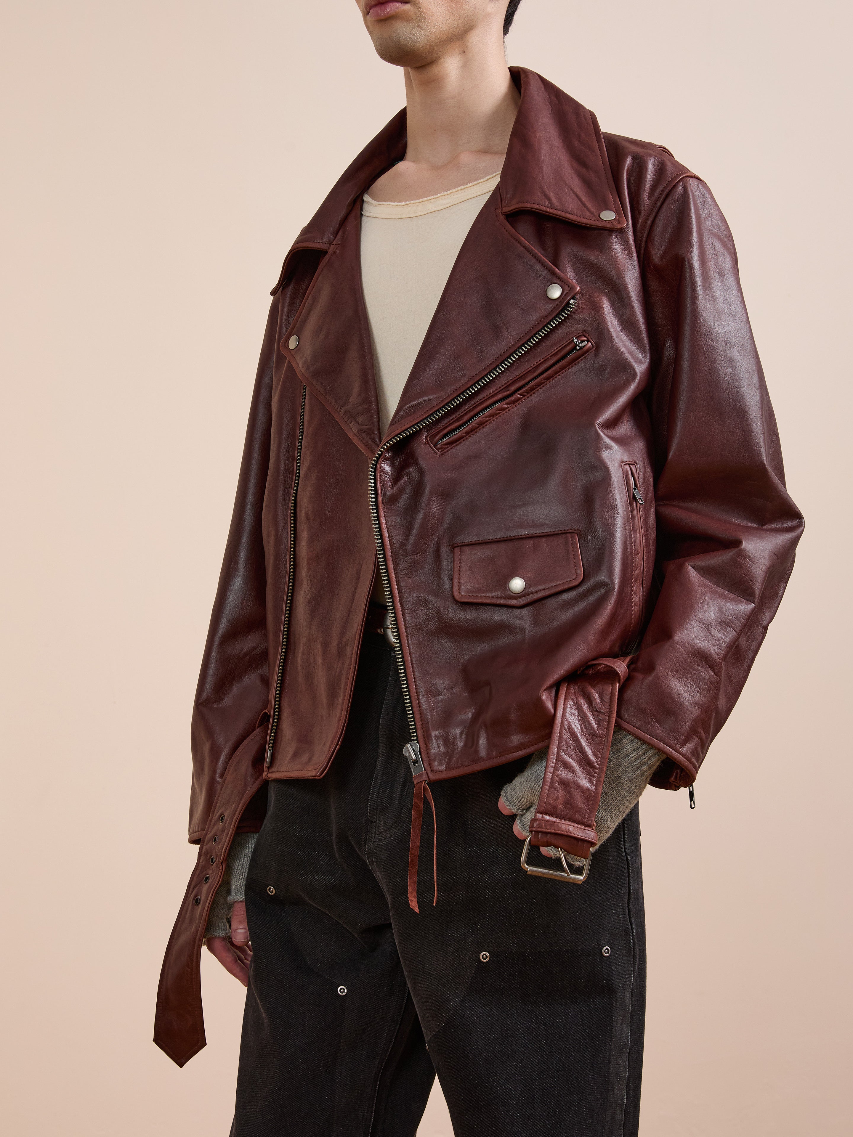 A person models the FOUND Leather Biker Jacket, layered over a beige shirt and black pants, shown from the shoulders down against a plain background.