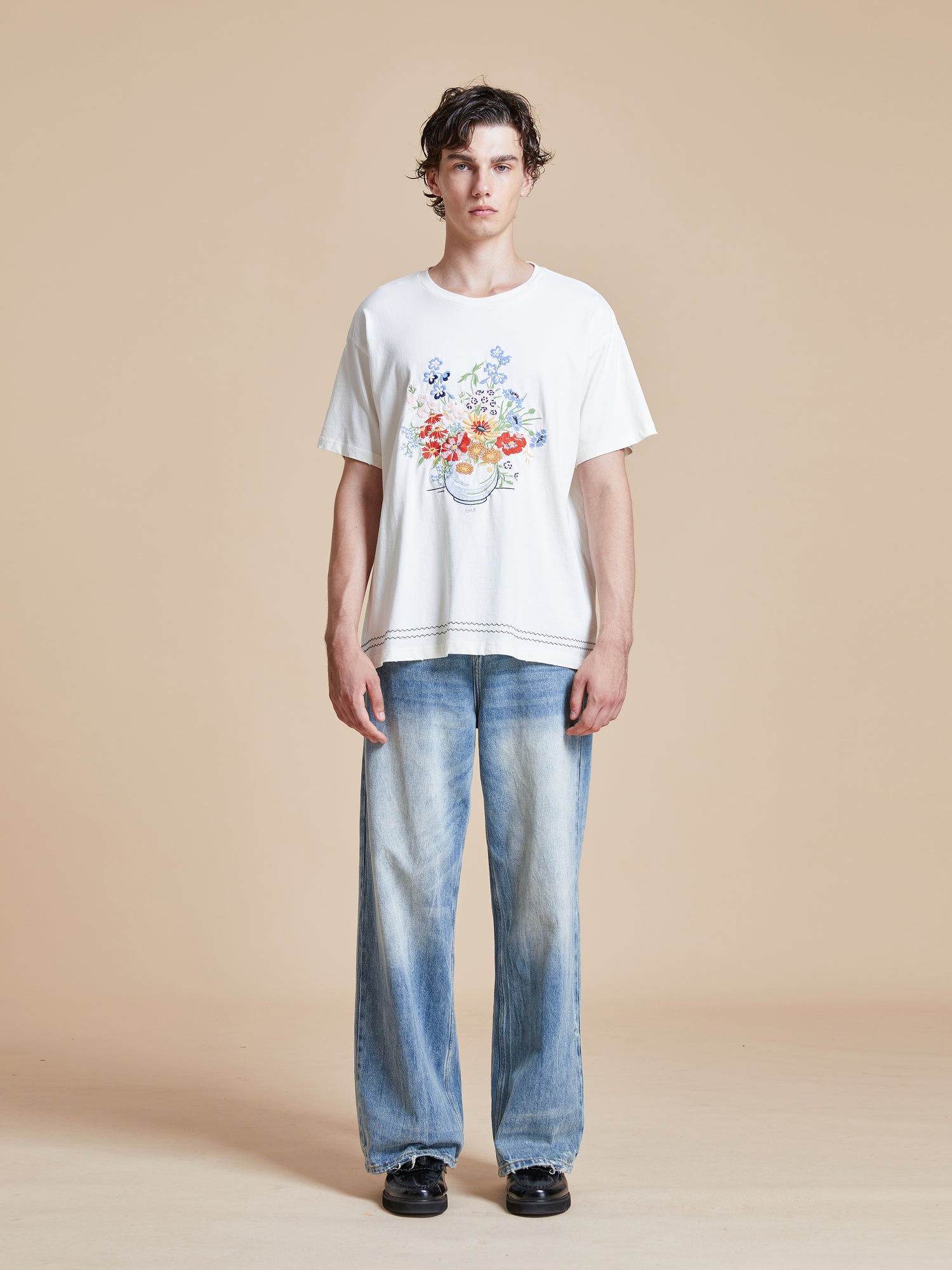 A man wearing a Bouquet Flowers Tee from Found and blue jeans.