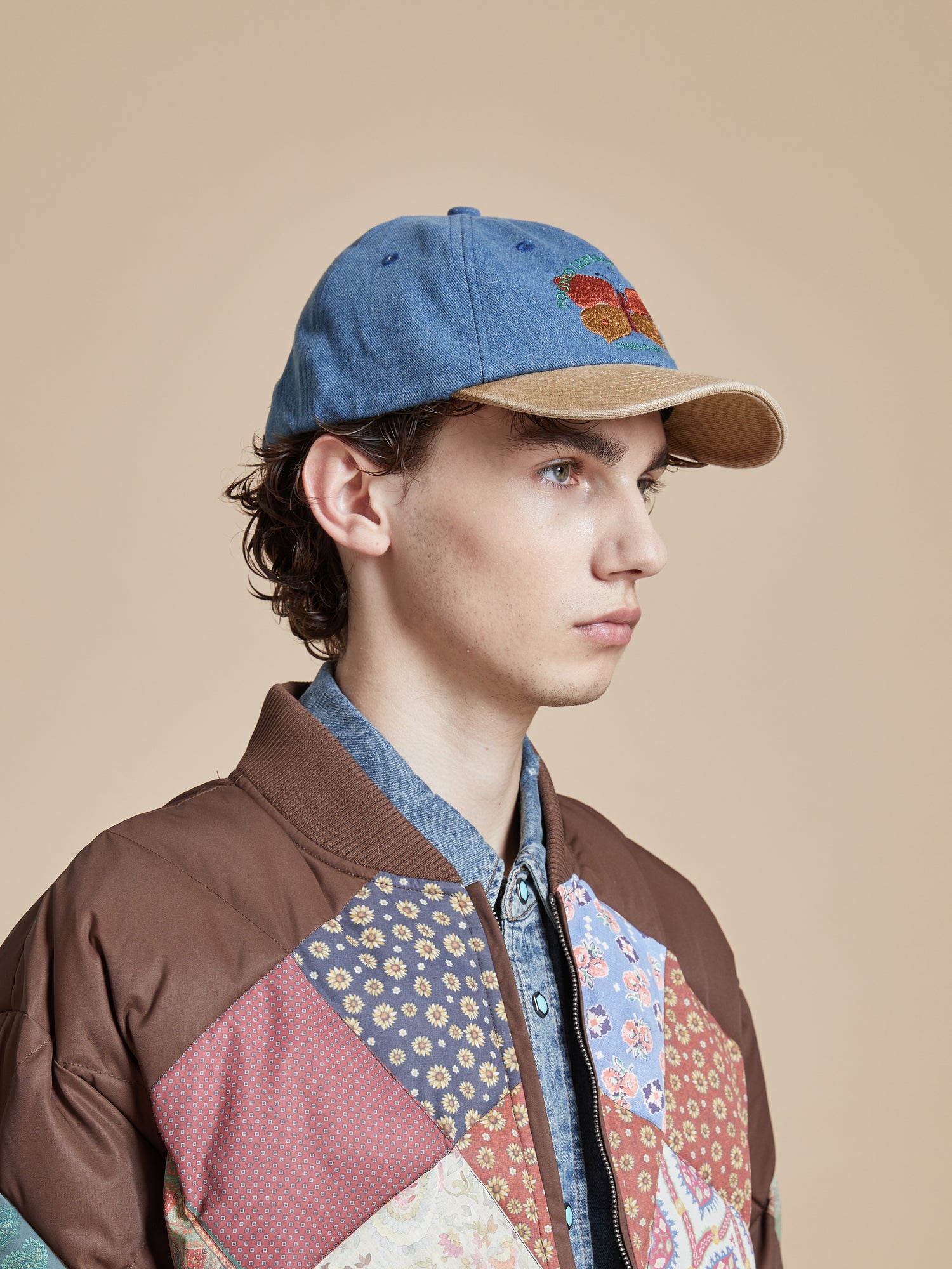 A young man wearing a Found Butterfly House Denim Cap and patchwork hat.