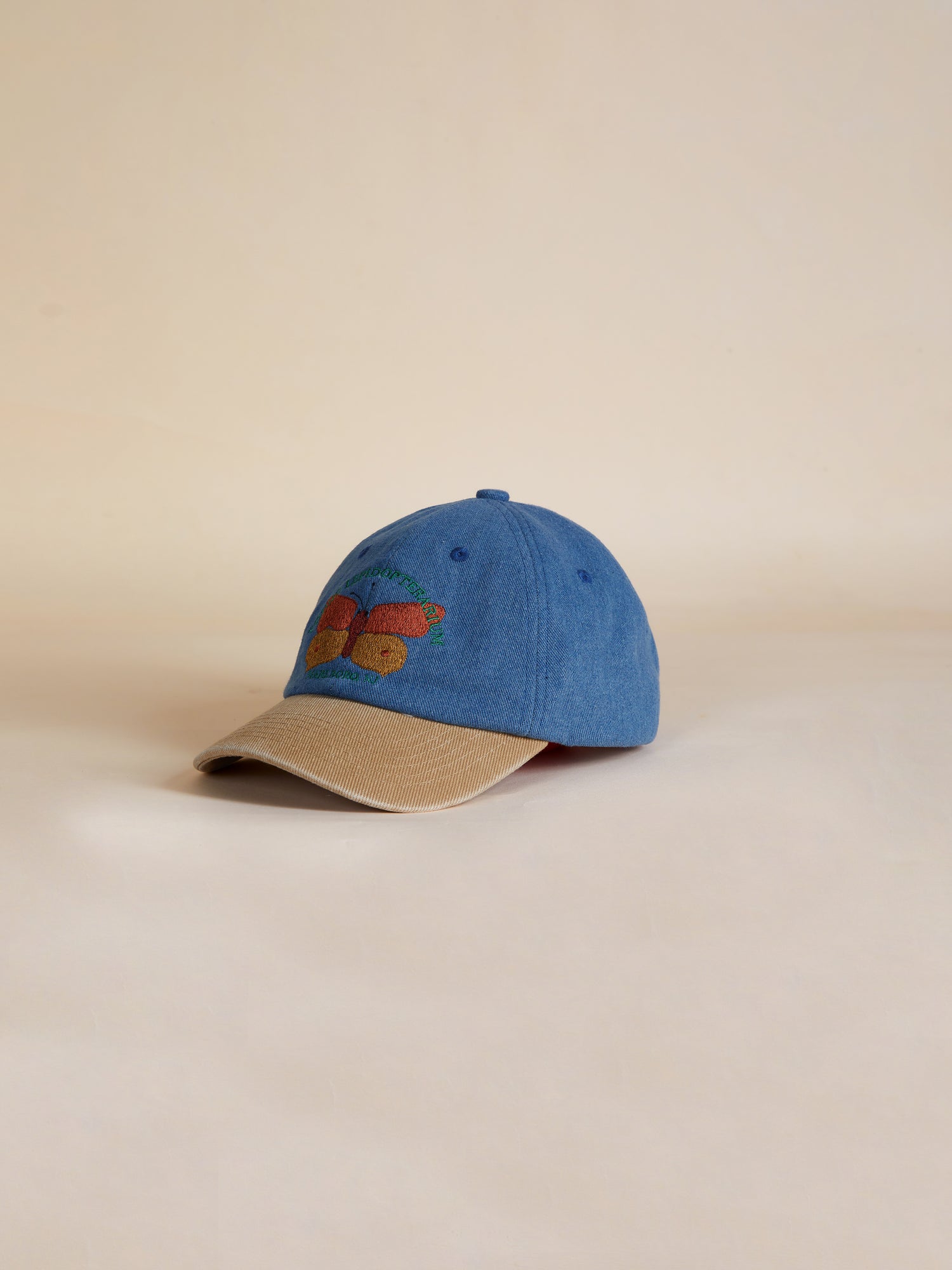 A blue and tan Butterfly House Denim Cap with an embroidered bird on it, by Found.