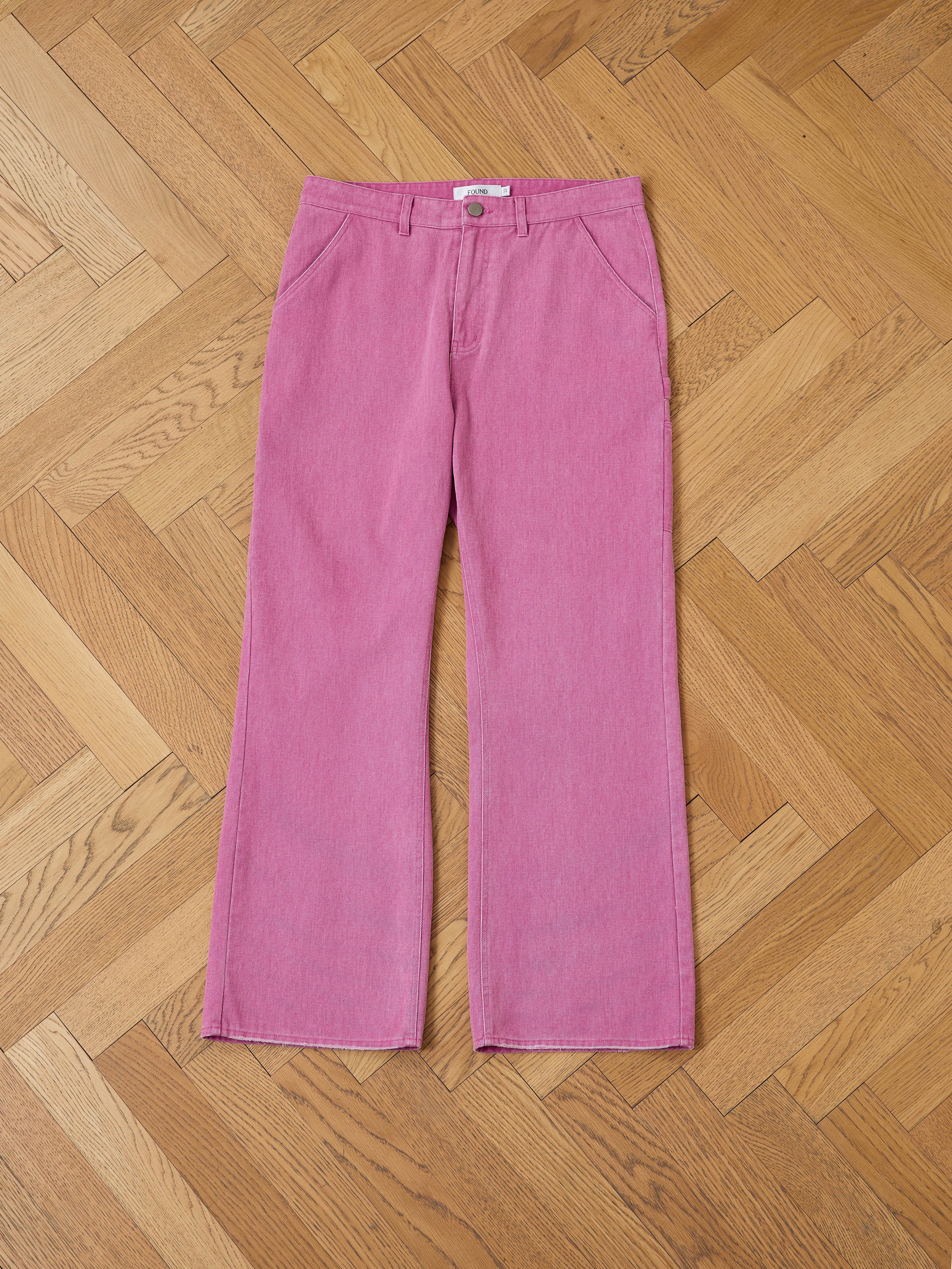 A pair of FOUND Flare Work Pants in pink with a high waist and relaxed fit is laid flat on a light wood chevron-patterned floor.