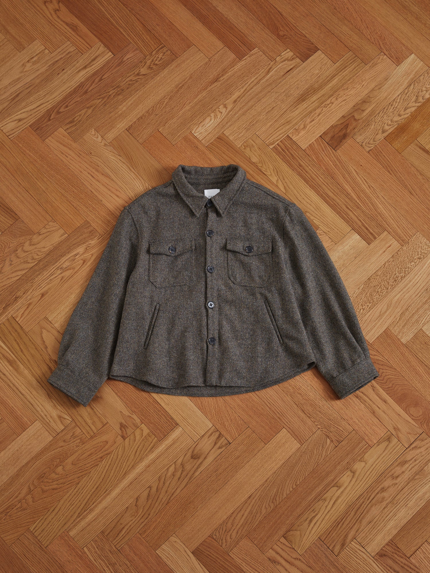A Raven Herringbone Overshirt by Found on a wooden floor.