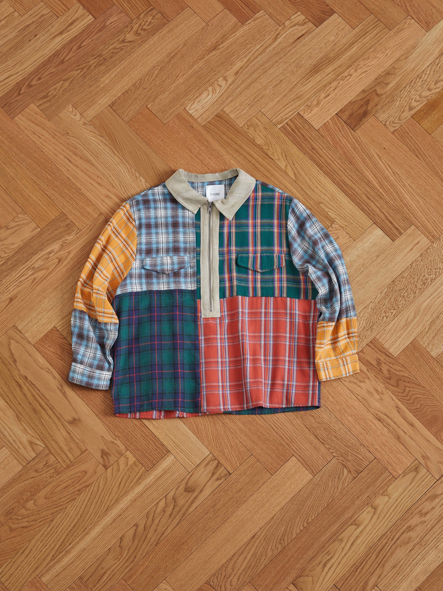A Found Multi Plaid Tartan Shirt with handcrafted distressing laying on a wooden floor.