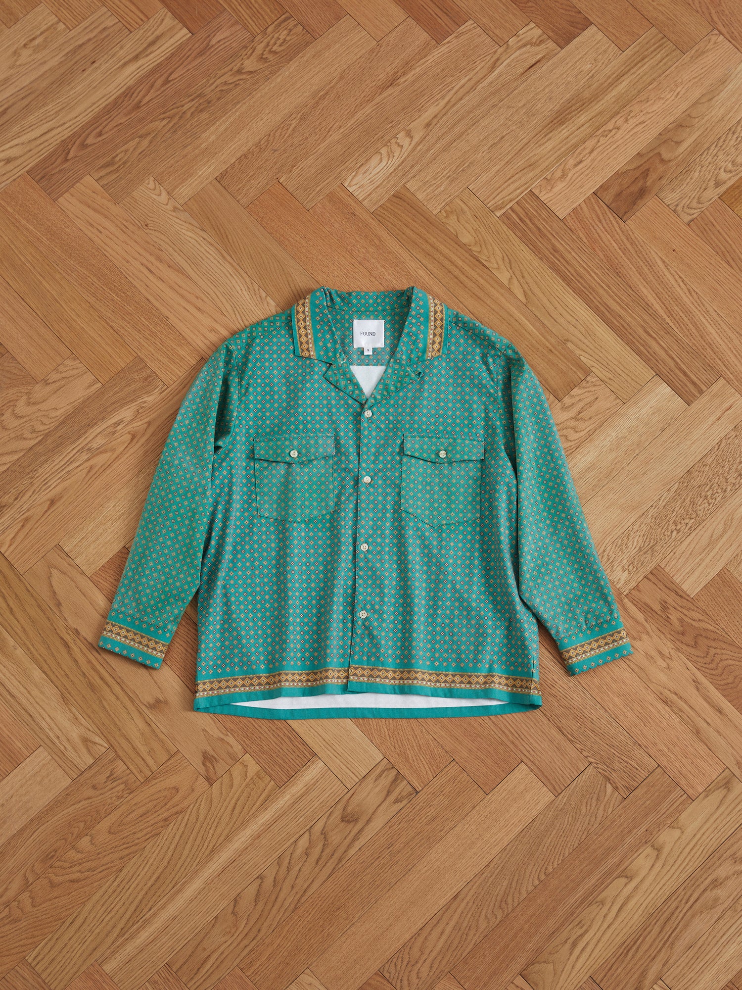 A Found Arbor Long Sleeve Camp Shirt with indo patterns lies on a wooden floor.