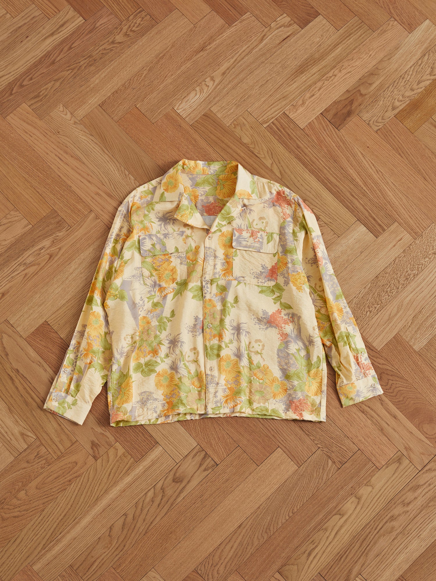 A yellow floral Found Meraj Vase Pot Long Sleeve Camp Shirt on a wooden floor, featuring Phulkari motifs from Punjab.