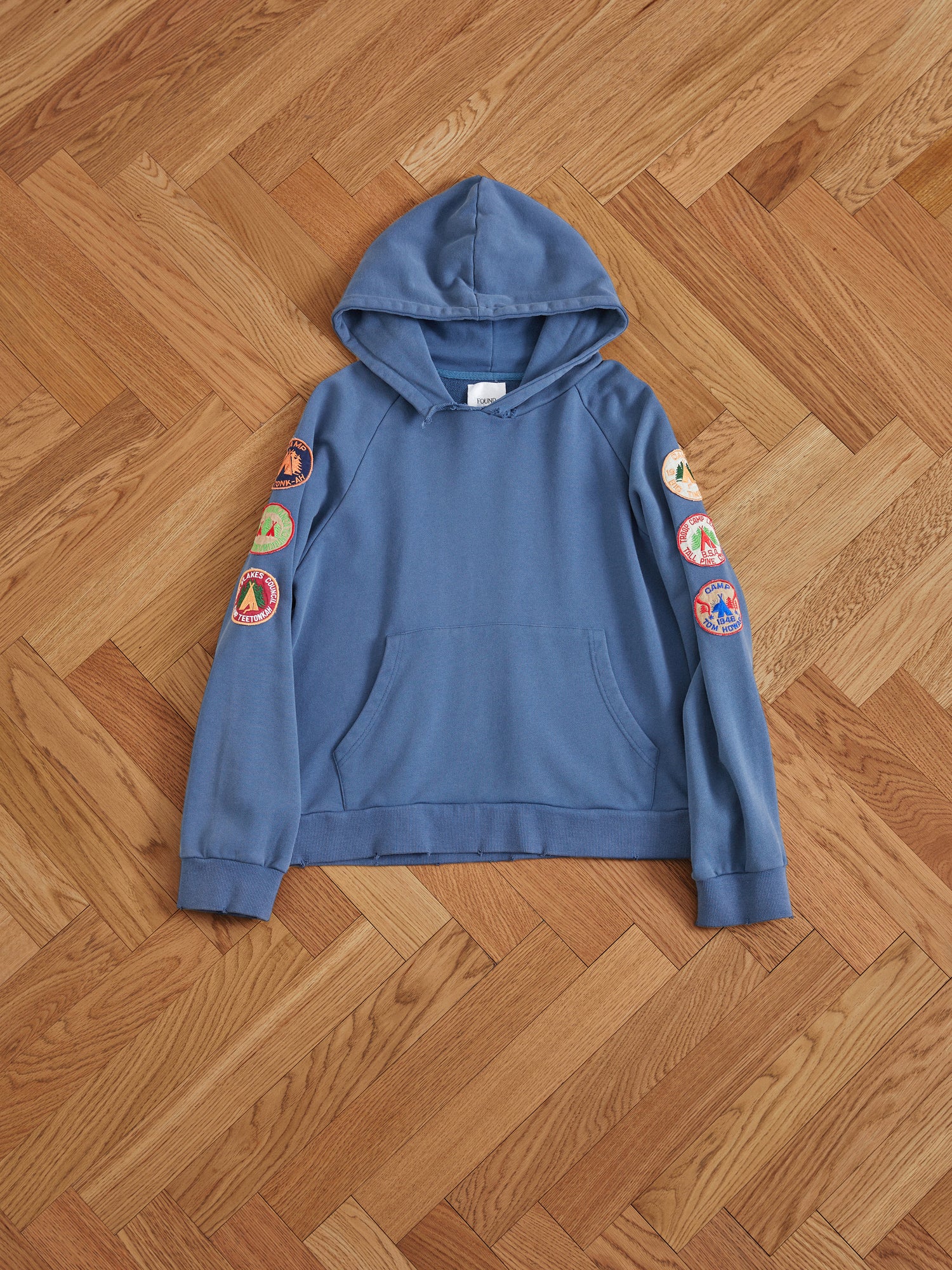 A vintage-inspired Found Timber Campground Hoodie in blue with patches on the front.
