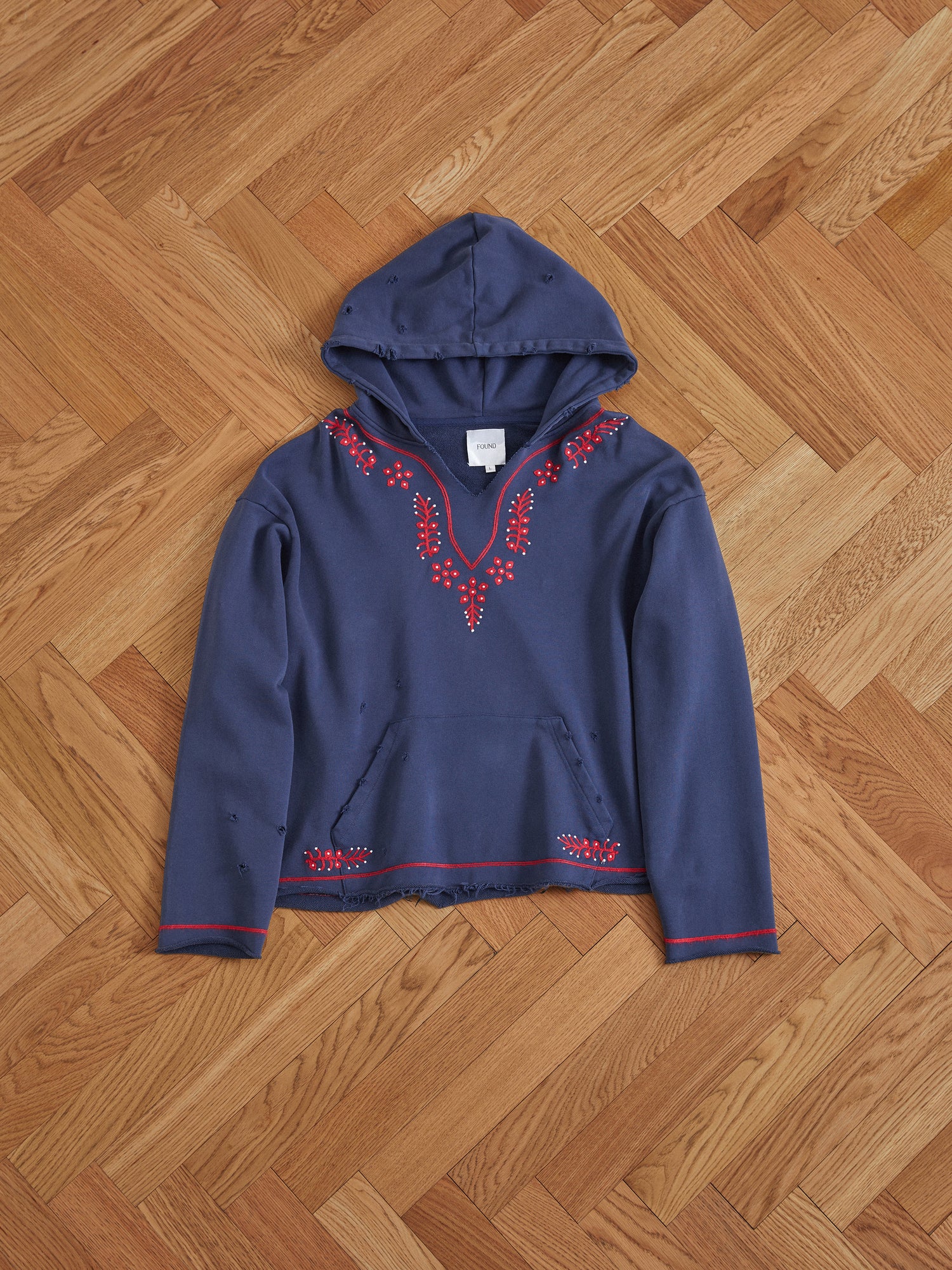 An Indus Embroidered Hoodie in blue on a wooden floor by Found.