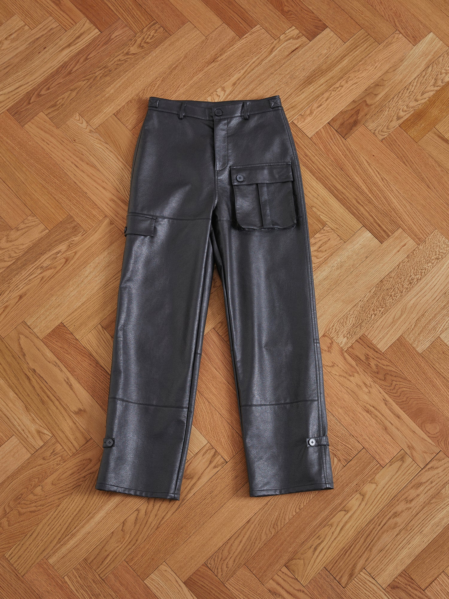 A pair of black Found faux leather cargo pants with cargo pockets on a wooden floor.
