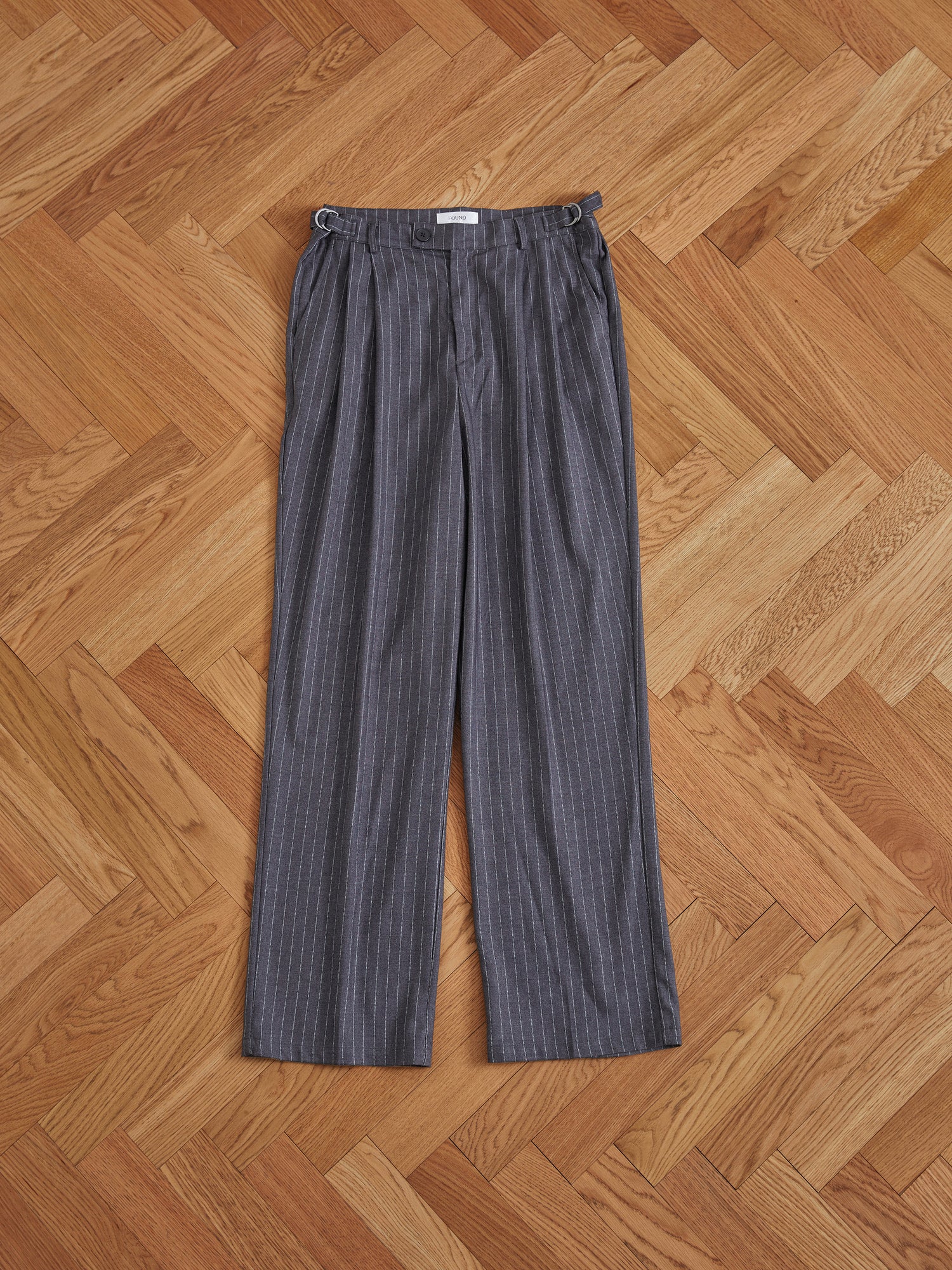 A pair of Found Pinstripe Pleated Trousers on a wooden floor.