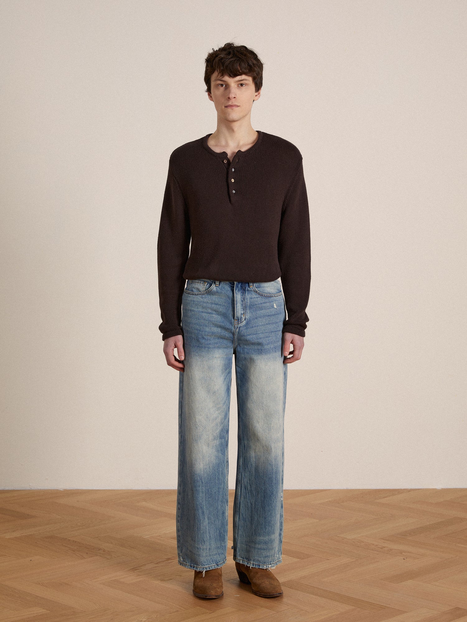 A man wearing jeans and a Profound Knit Henley sweater standing on a wooden floor.