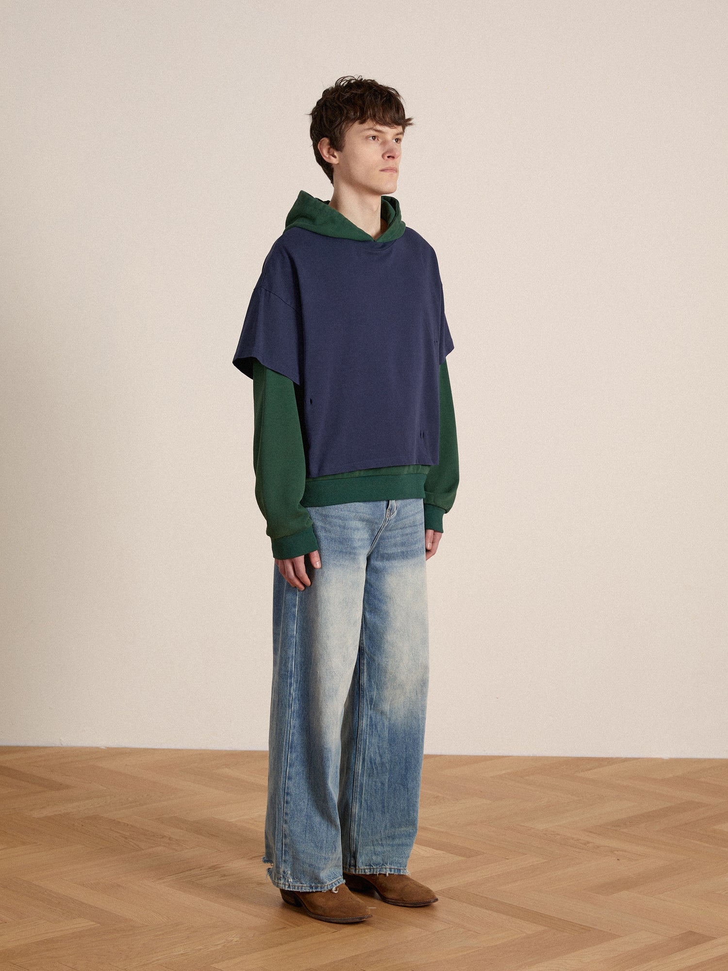 A man wearing Lacy Baggy Jeans and a Found Double Layer Hoodie standing on a wooden floor.