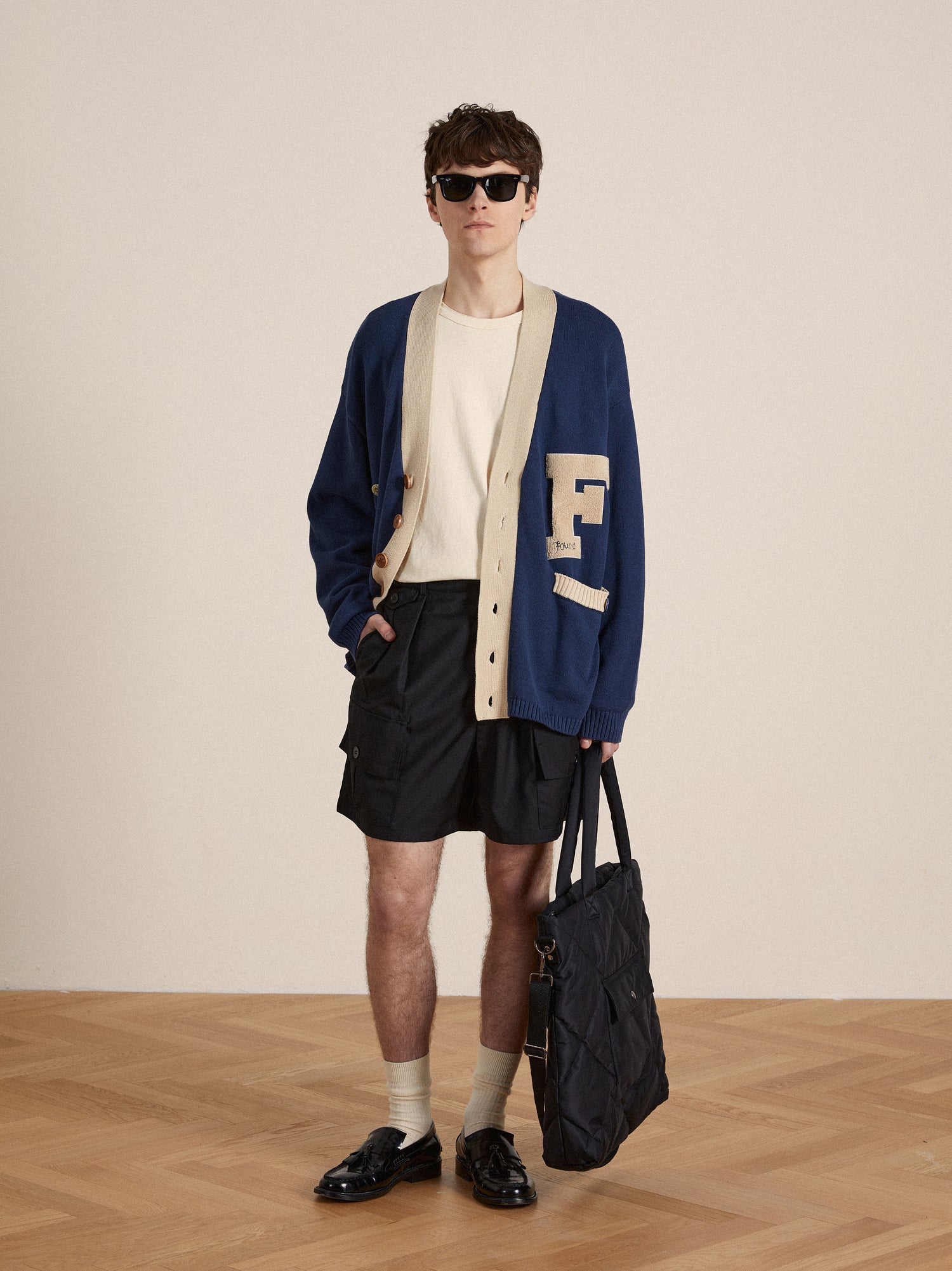 A man in a Found Varsity Contrast Cardigan and shorts holding a bag.