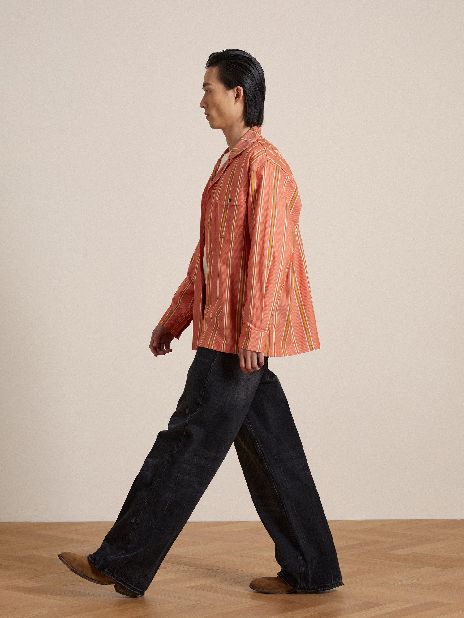 A man in a Found Stripe Citrus LS Camp Shirt with classic appeal walking across a wooden floor.