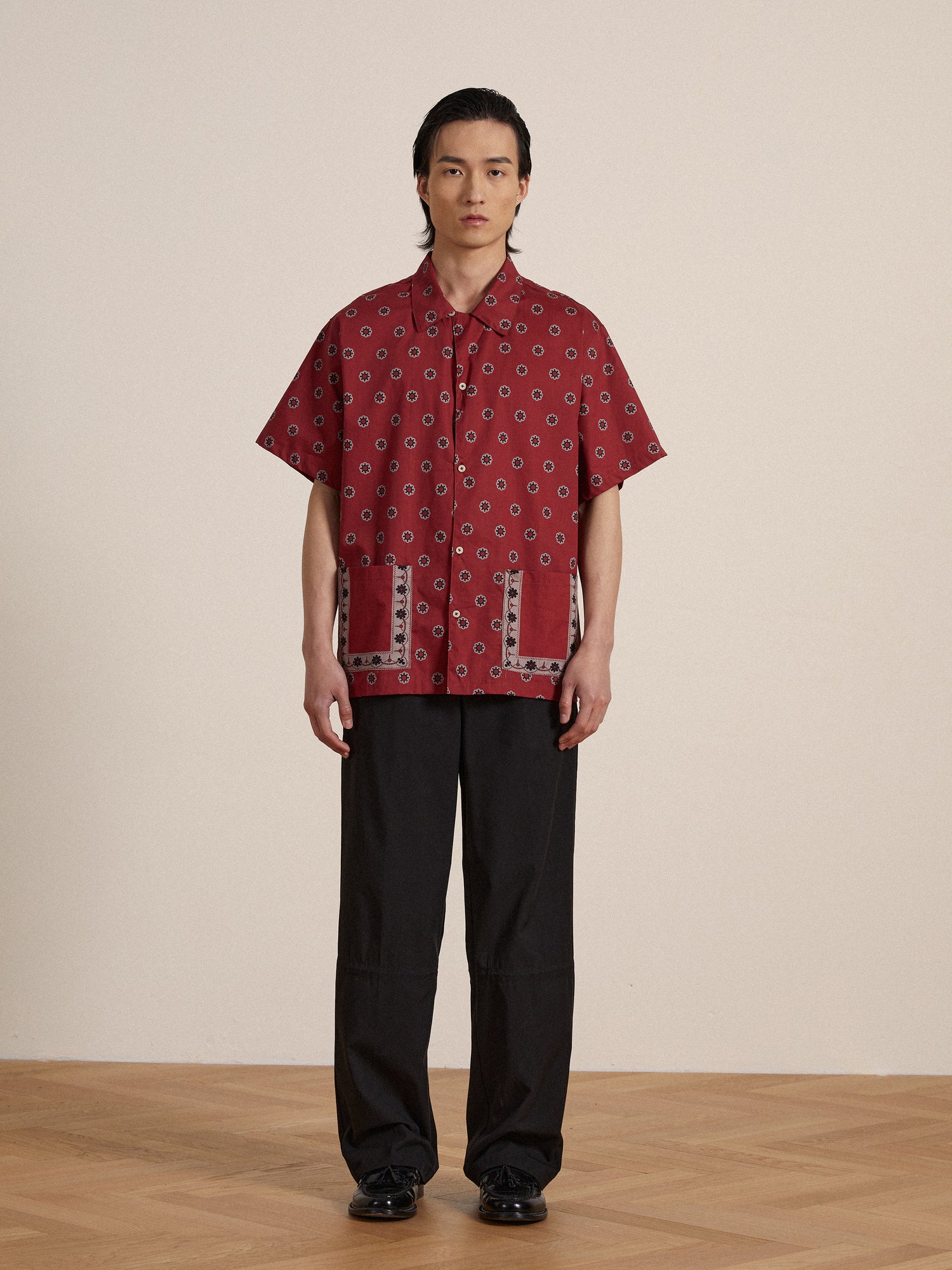 A man wearing a Found Red Motif SS Camp Shirt and black pants.