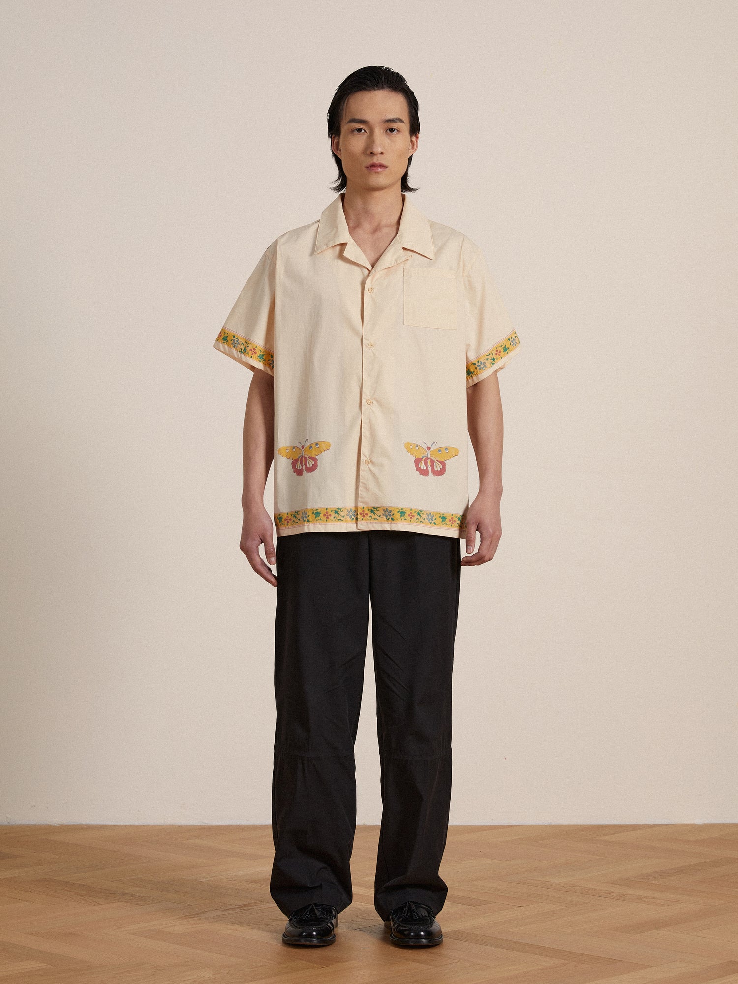 A man wearing a yellow Found Moth Camp Shirt and black Nylon Pleated Pants.