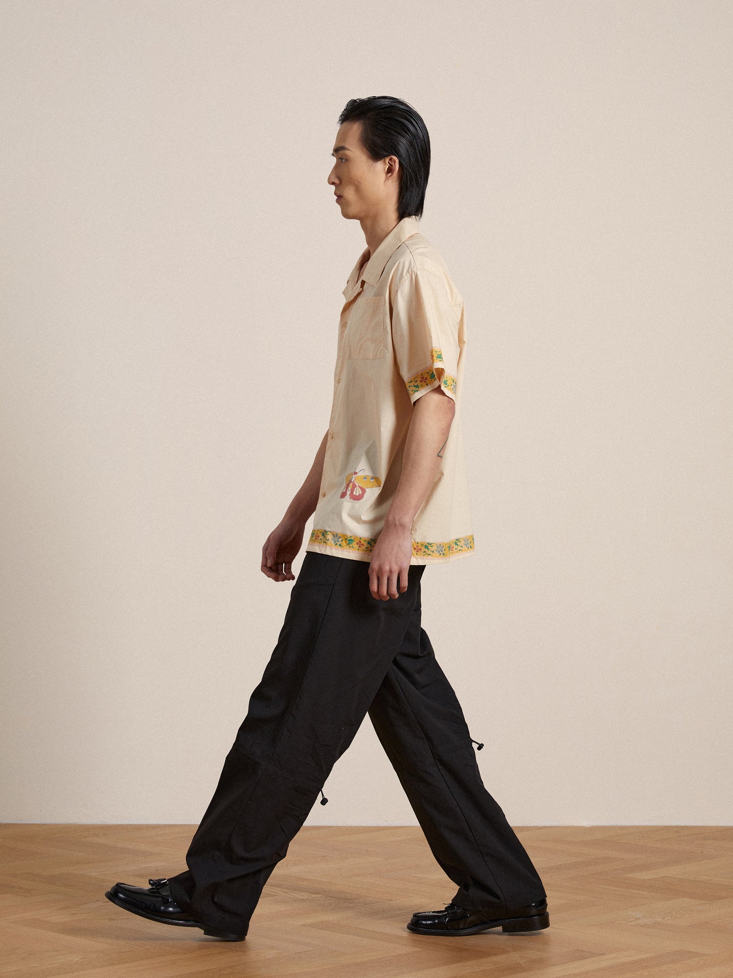 A man in a Found Moth Camp Shirt and black pants walking on a wooden floor.