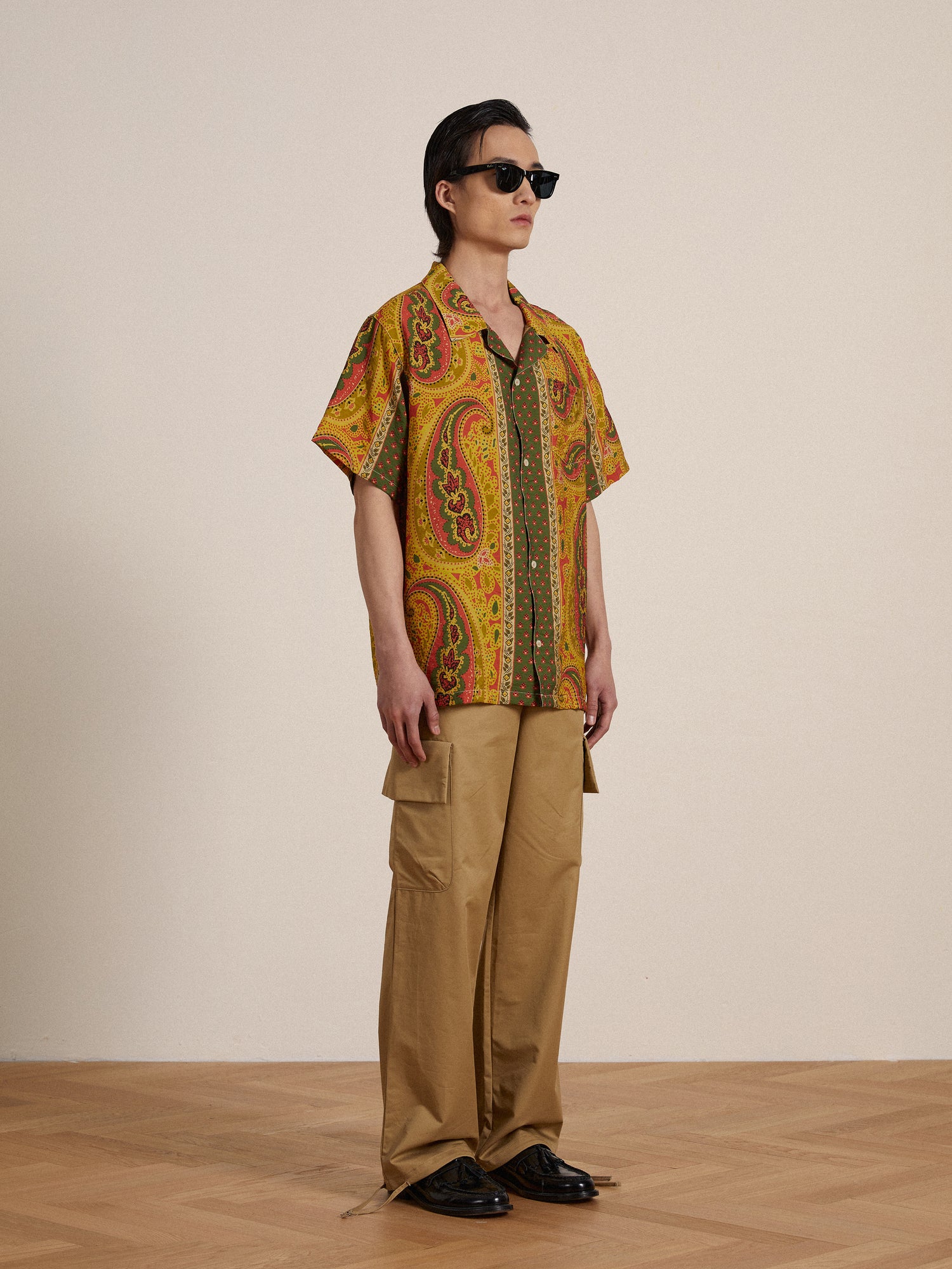 A man wearing a Found Pench Paisley SS Camp Shirt with paisley prints and khaki pants.