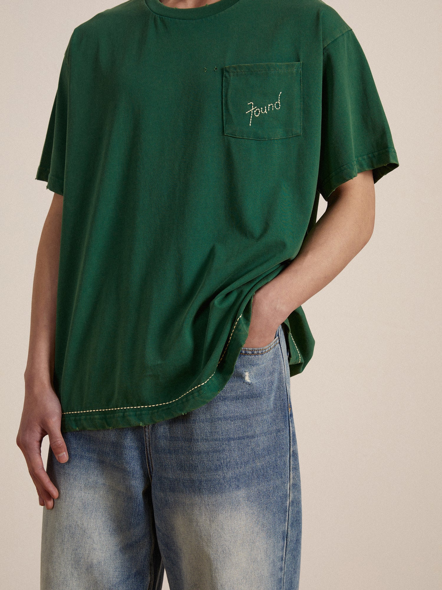 A man wearing a green Found Embroidered Logo Tee and jeans.