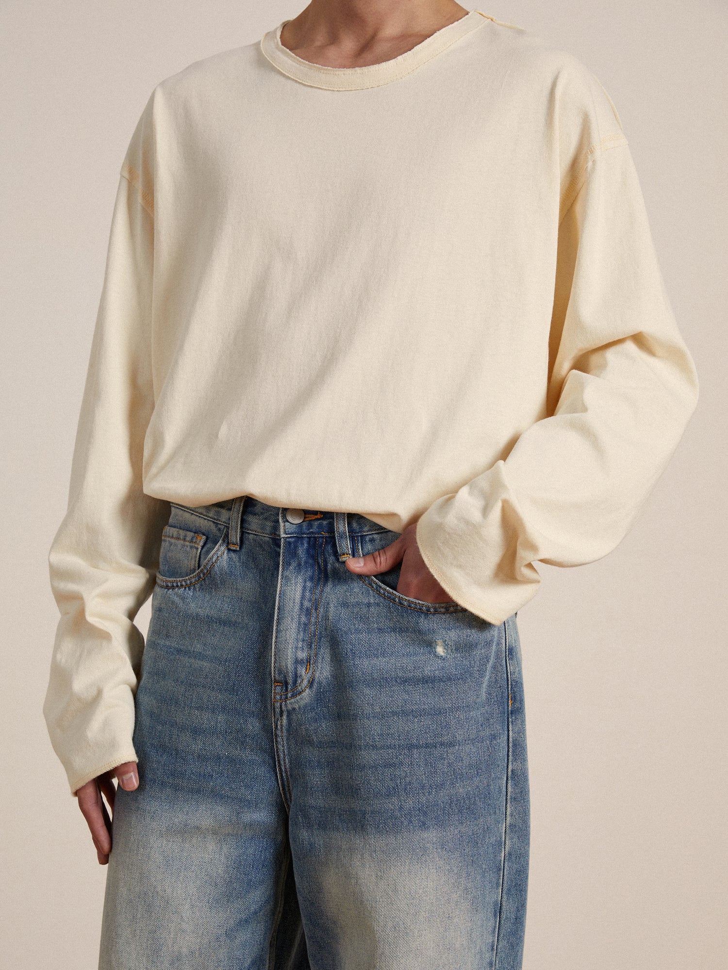 A man wearing jeans and a cream long-sleeved Reversed LS Tee made of premium materials with reversed seams from Profound.