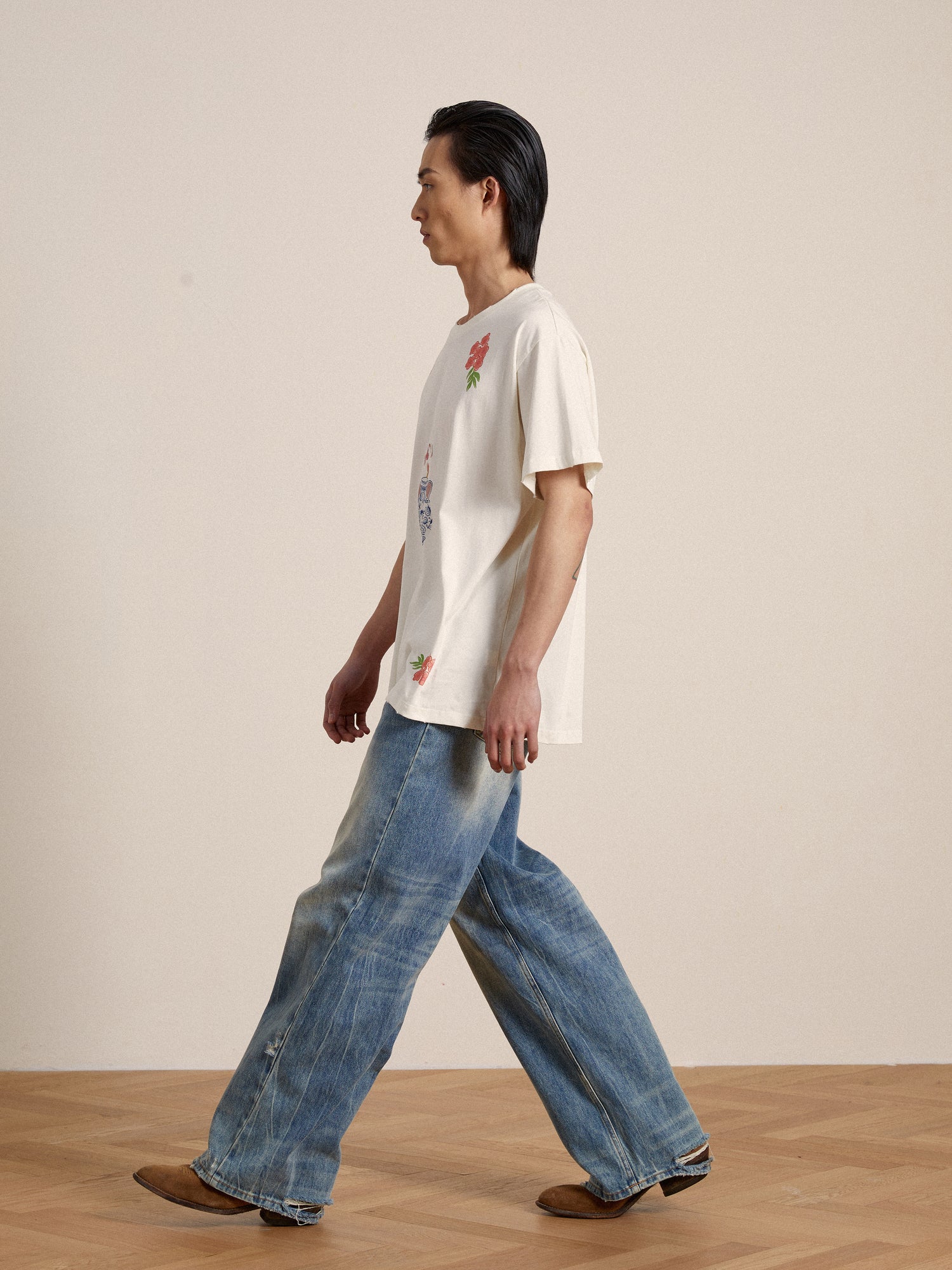 A man wearing a Found Flower Pot Tee and jeans walking on a wooden floor.